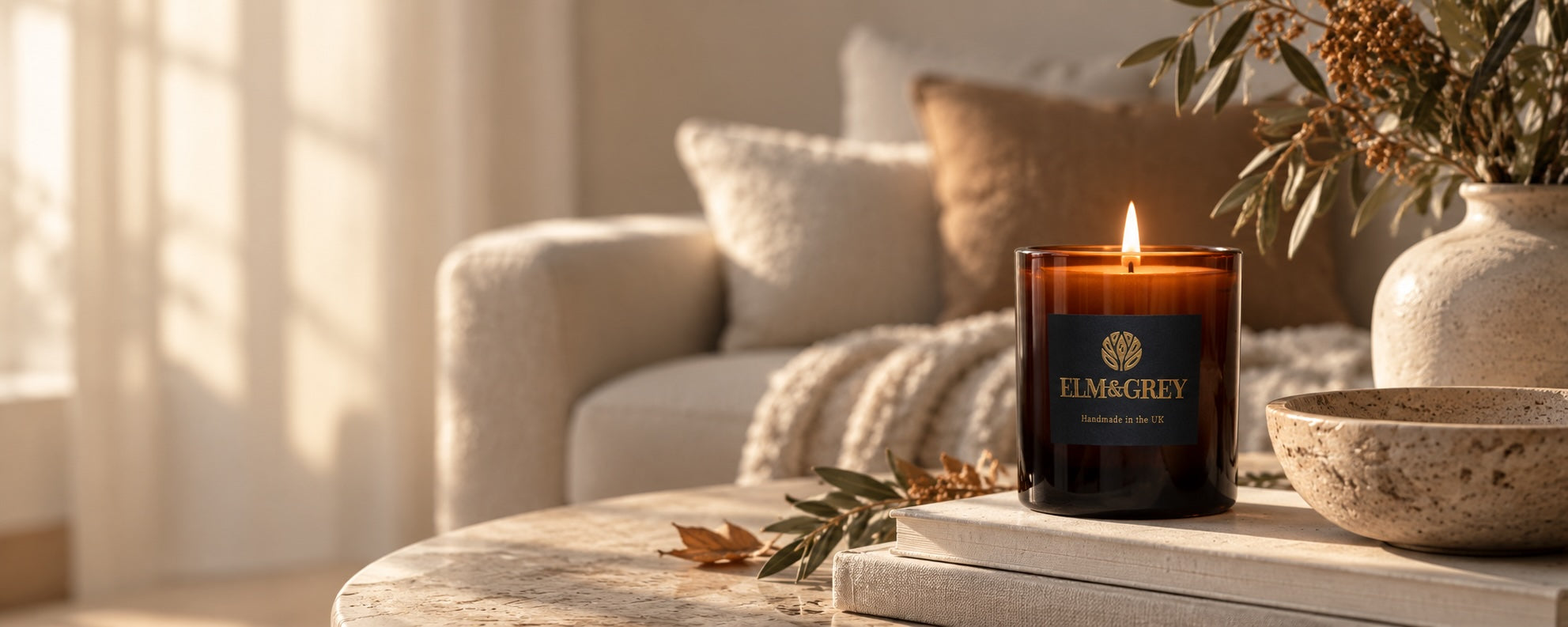 Elm & Grey amber glass candle styled on a neutral coffee table with autumn foliage, stone accessories and soft warm light