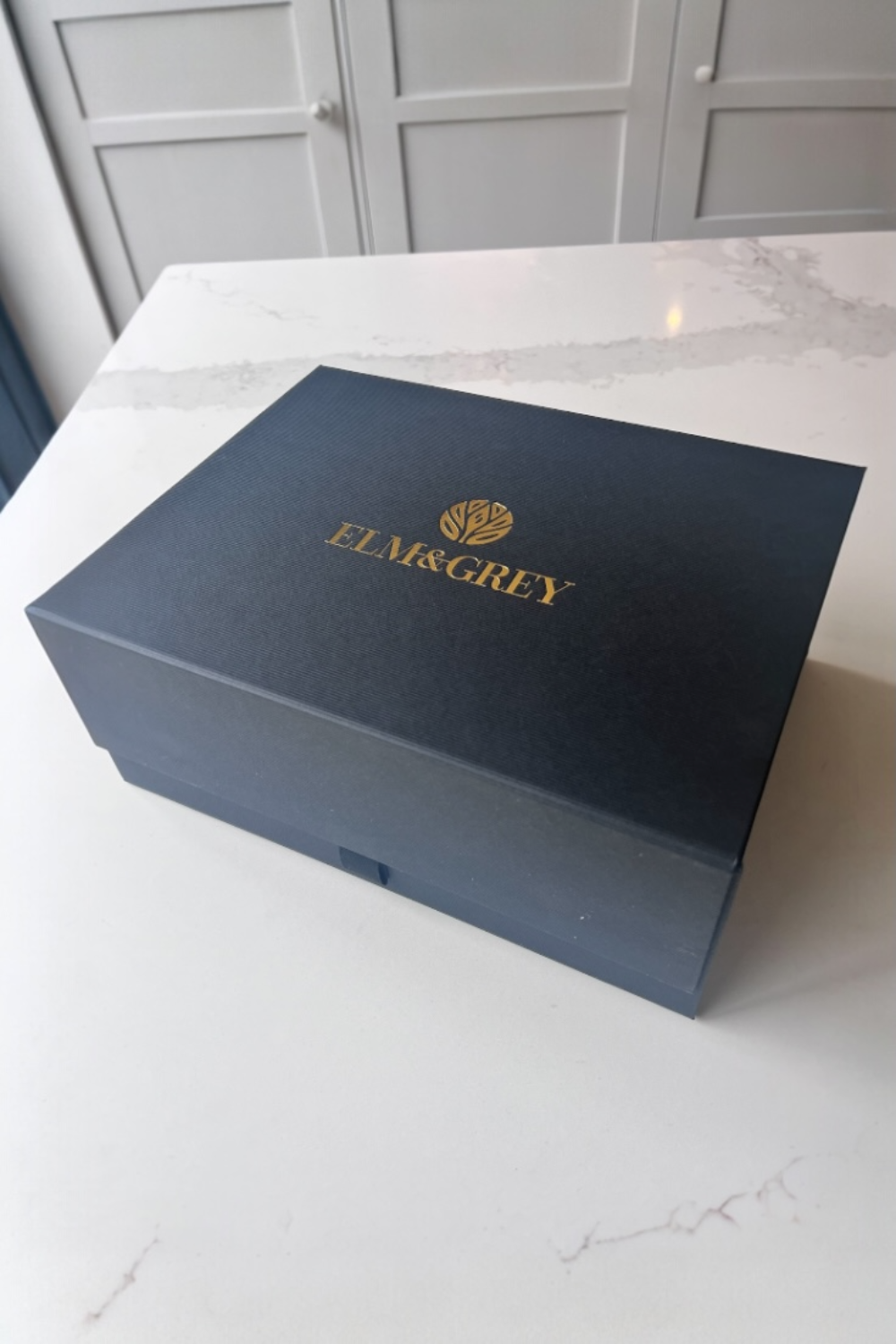 Black box with gold ELM&GREY branding on a white surface