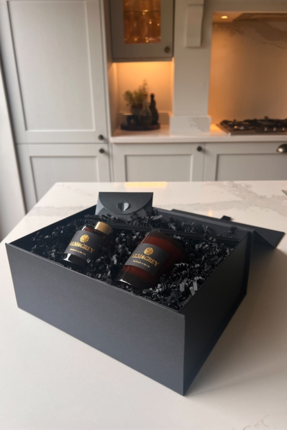 Elm & Grey Scent Ritual Gift Box open showing candle and diffuser nestled in black crinkle paper with message card on marble countertop