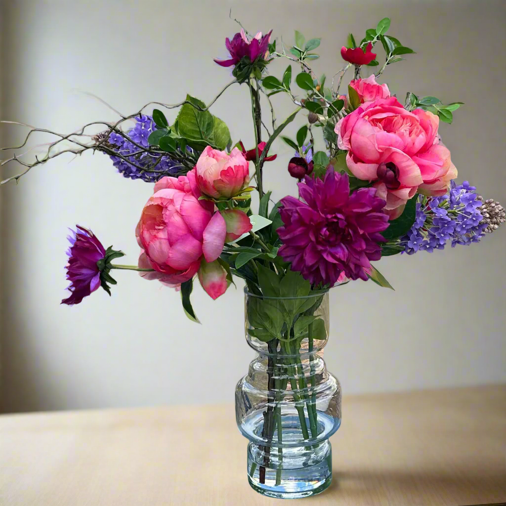 Bouquet of pink, purple, and red flowers in a clear glass vase on a neutral background