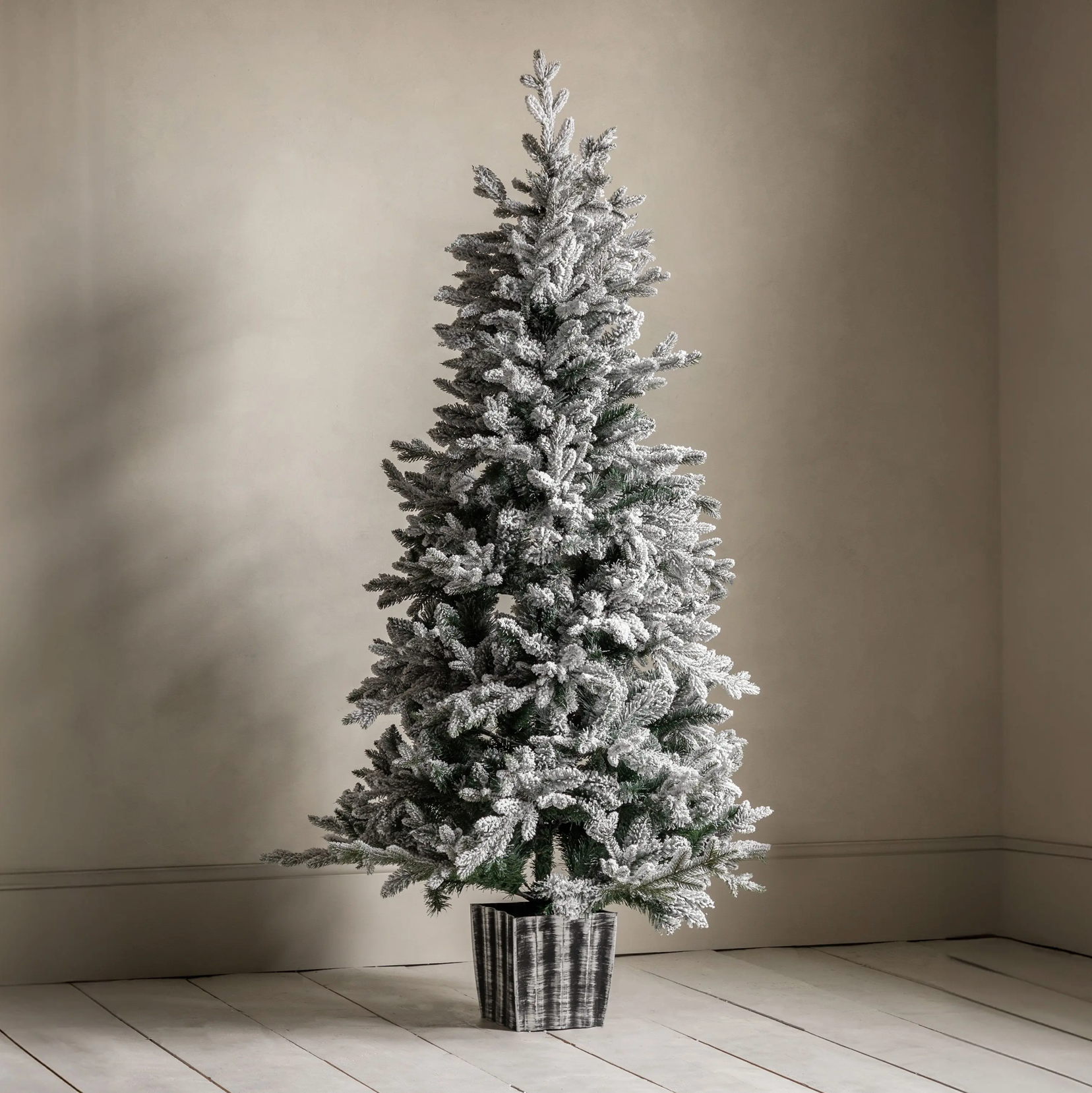 Frosted Christmas tree in a pot on a wooden floor with a beige wall background