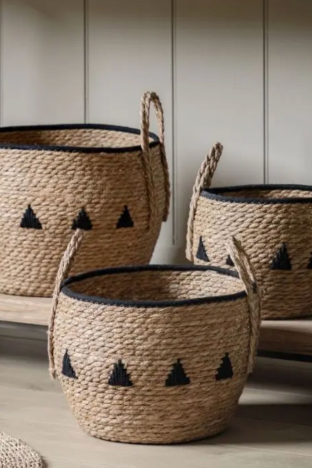 Three woven baskets with black triangular patterns on a wooden surface.