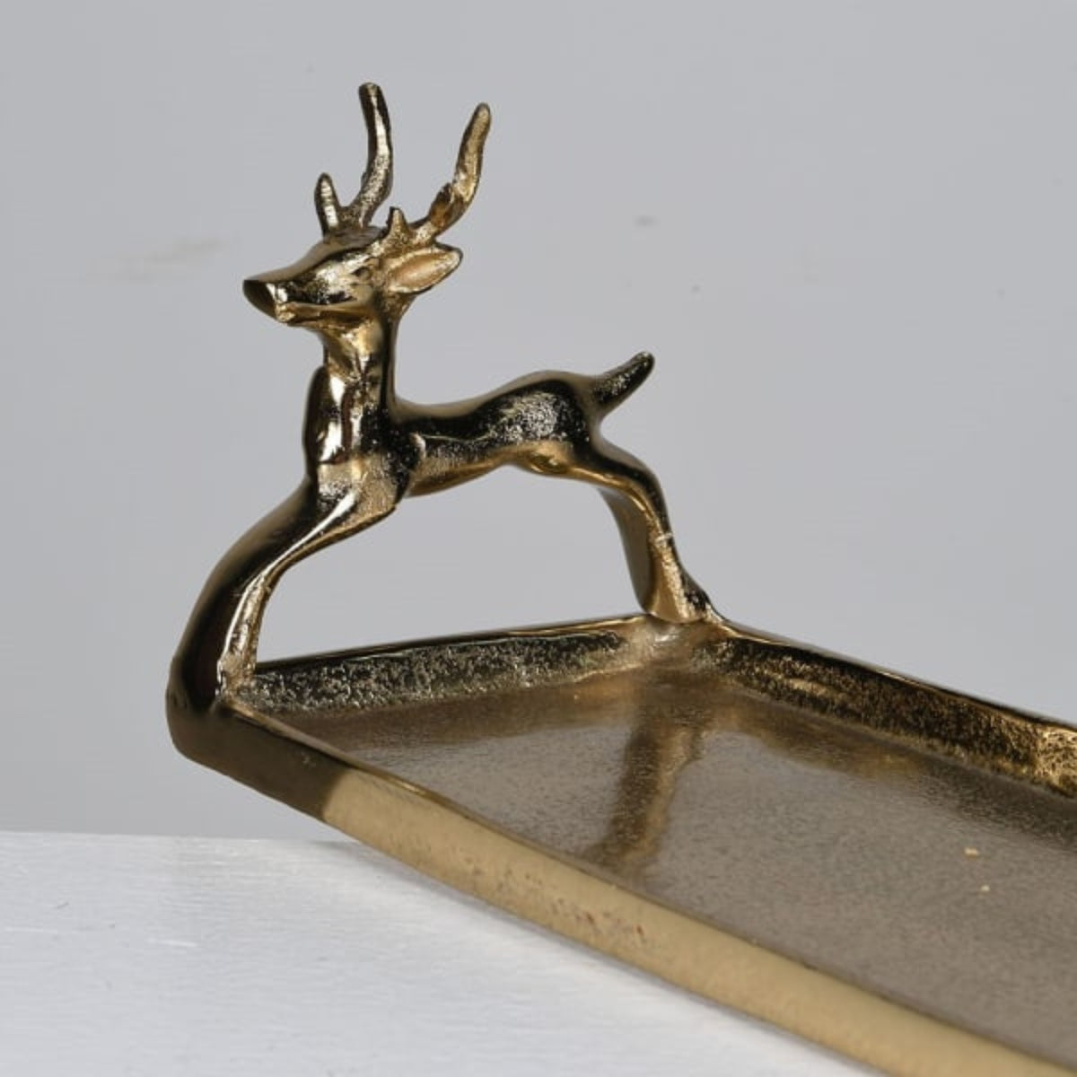 A rectangular tray with a polished metallic gold finish and a sculpted deer figure on the back edge, shown against a plain light gray background.