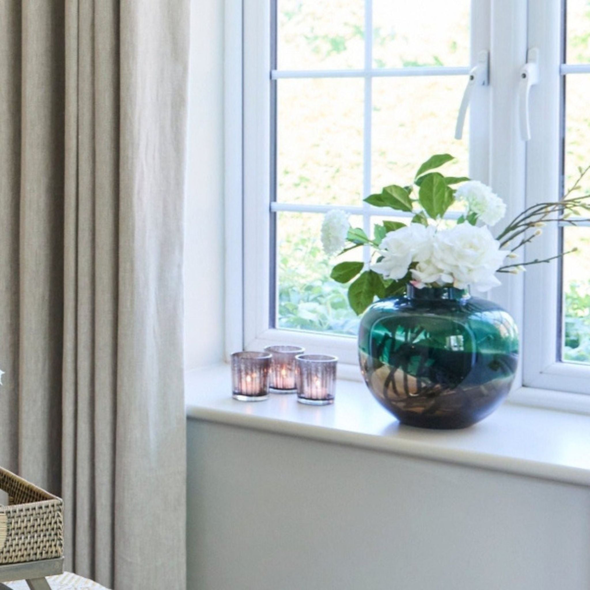 Decorative vase with flowers on a windowsill next to curtains