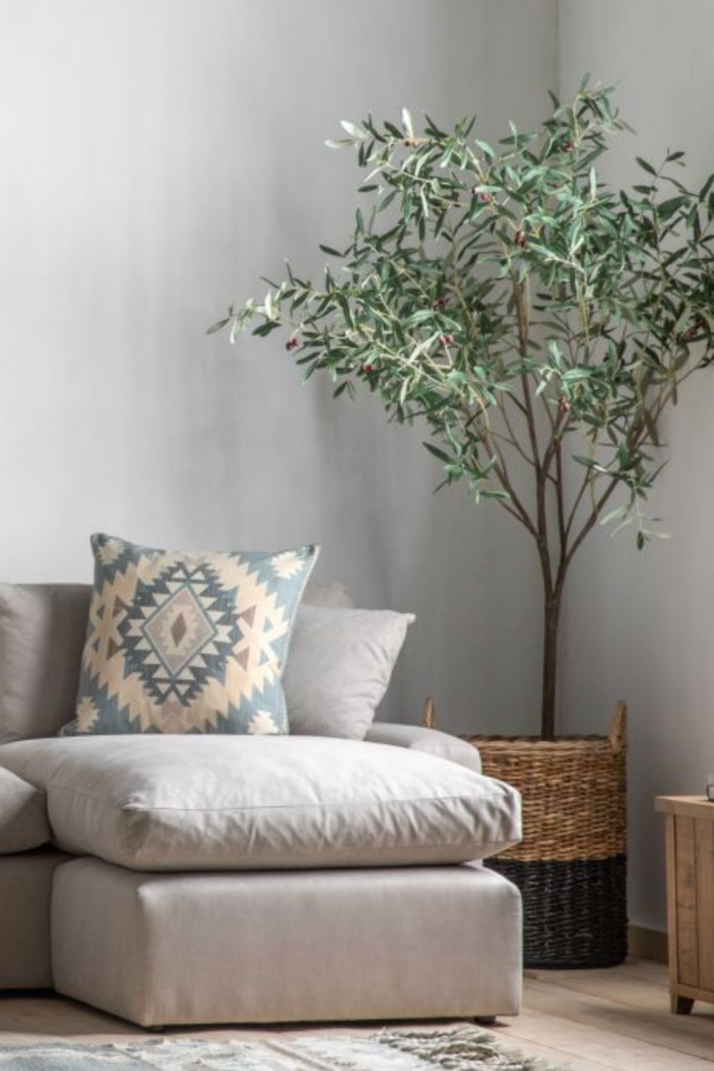 Grey sofa with a patterned pillow and a potted plant in a room with a neutral colour scheme.