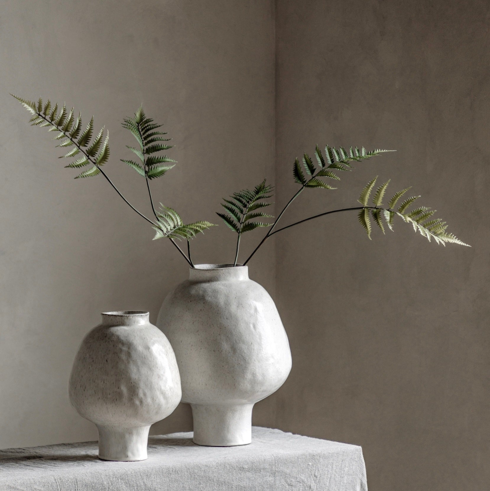 Two white textured vases with fern branches on a neutral background