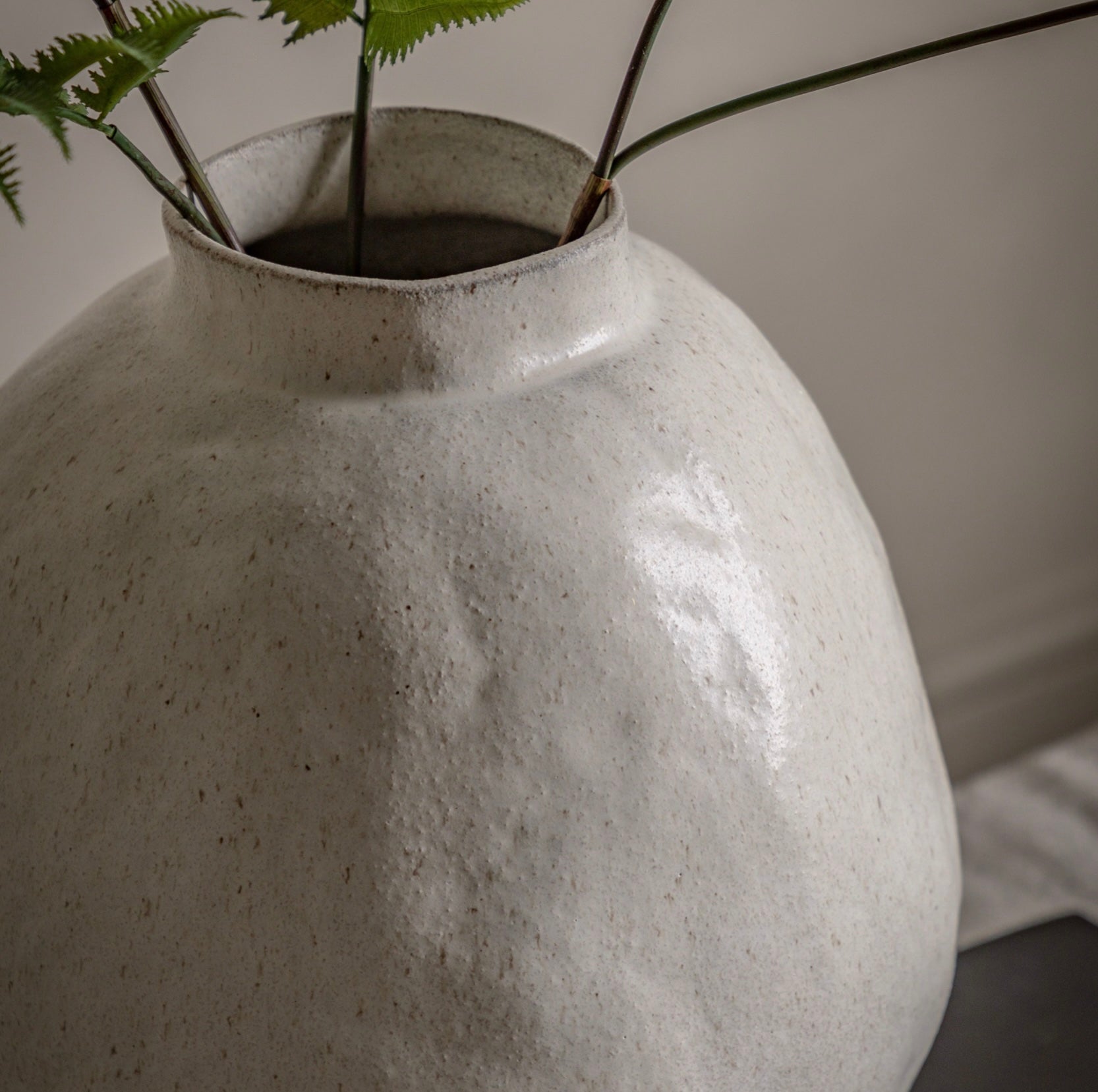 Sculptural stoneware vase with a plant against a neutral background