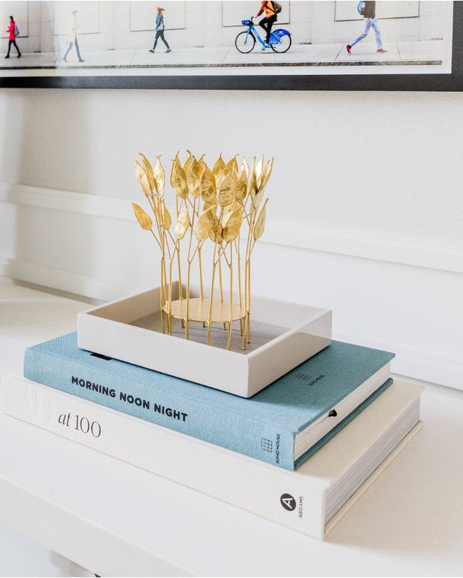 Latte high gloss lacquer square tray styled with gold botanical leaf sculpture on stacked coffee table books in a neutral panelled interior — Elm & Grey
