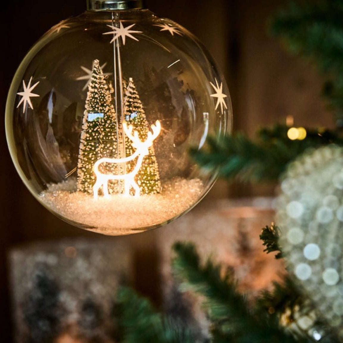 Decorative Christmas ornament with a reindeer and trees inside a glass ball, hanging on a tree.