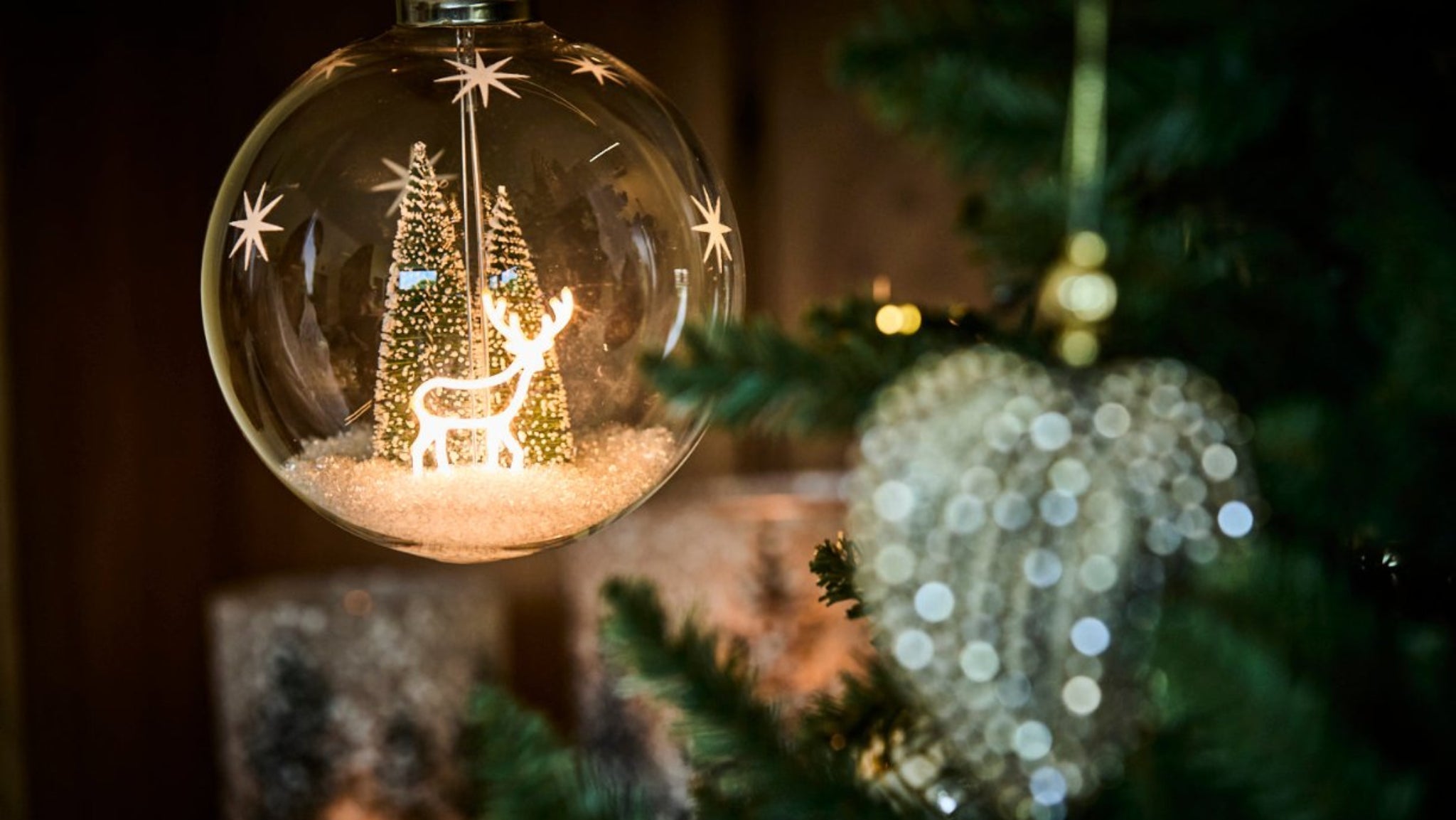 Decorative Christmas ornament with a reindeer and trees inside a glass ball, hanging on a tree.