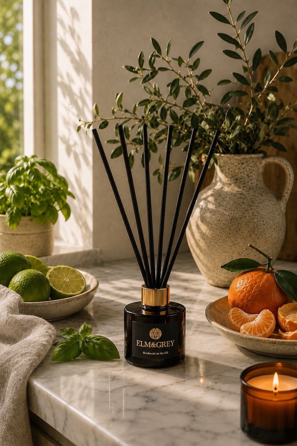 Elm & Grey diffuser on a marble surface with limes, oranges, and a lit candle.