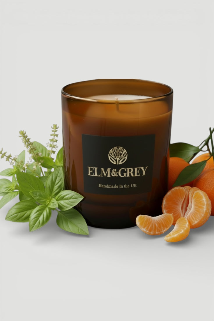 lime basil and mandarin Brown candle with 'ELM&GREY' branding surrounded by leaves and oranges on a light background