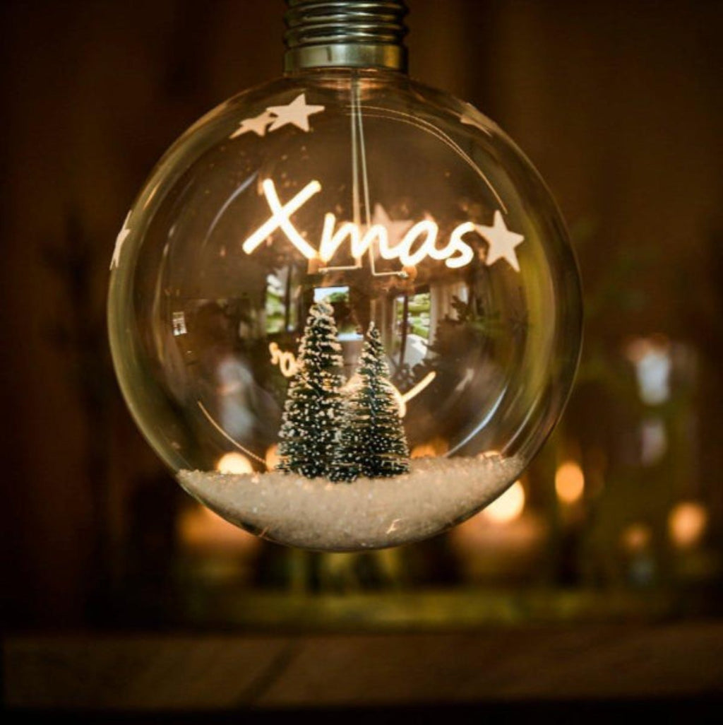 Decorative light bulb with 'Xmas' and Christmas tree inside, on a blurred background.
