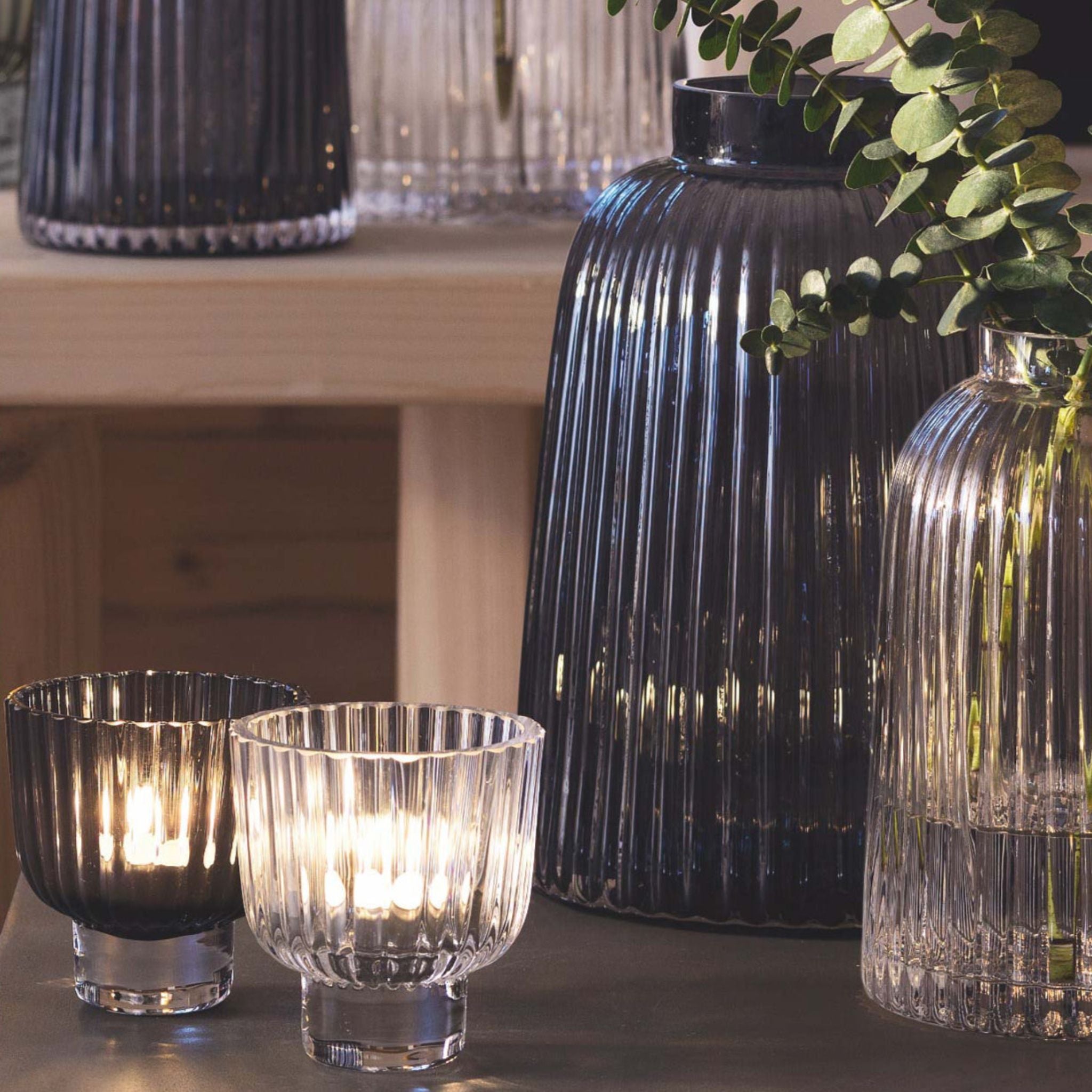 Decorative glassware including black ribbed vases and clear candle holders on a wooden surface.