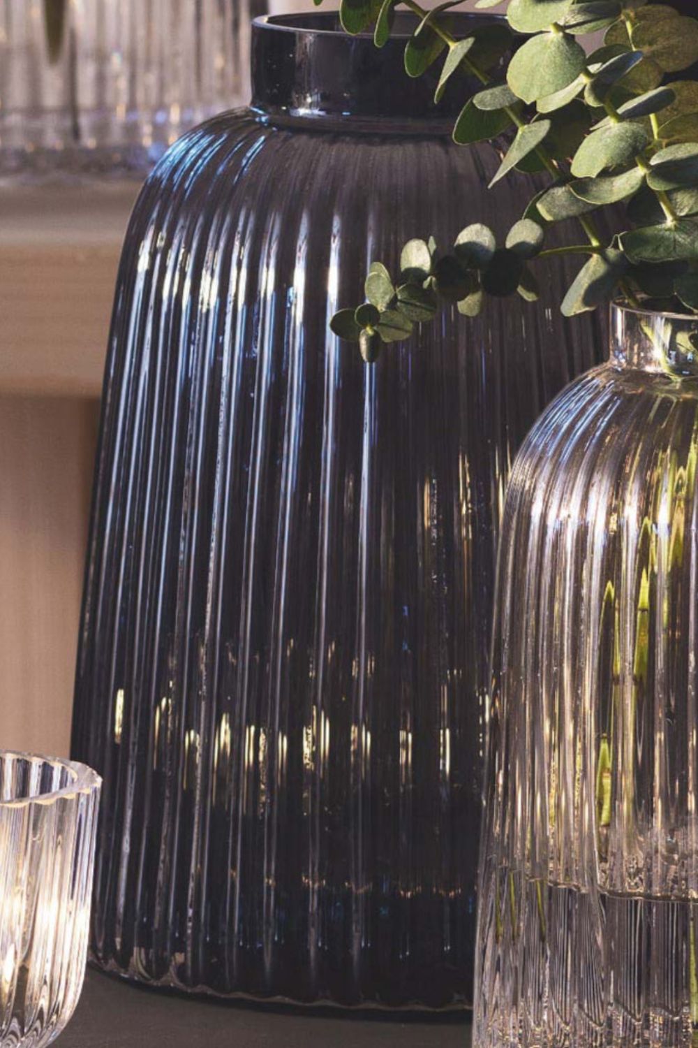 Decorative black ribbed vase with a clear glass vase and green leaves in the foreground.