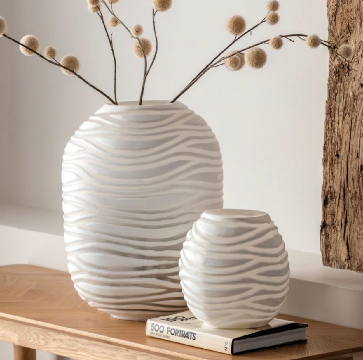 Two white textured vases on a wooden surface with a neutral background