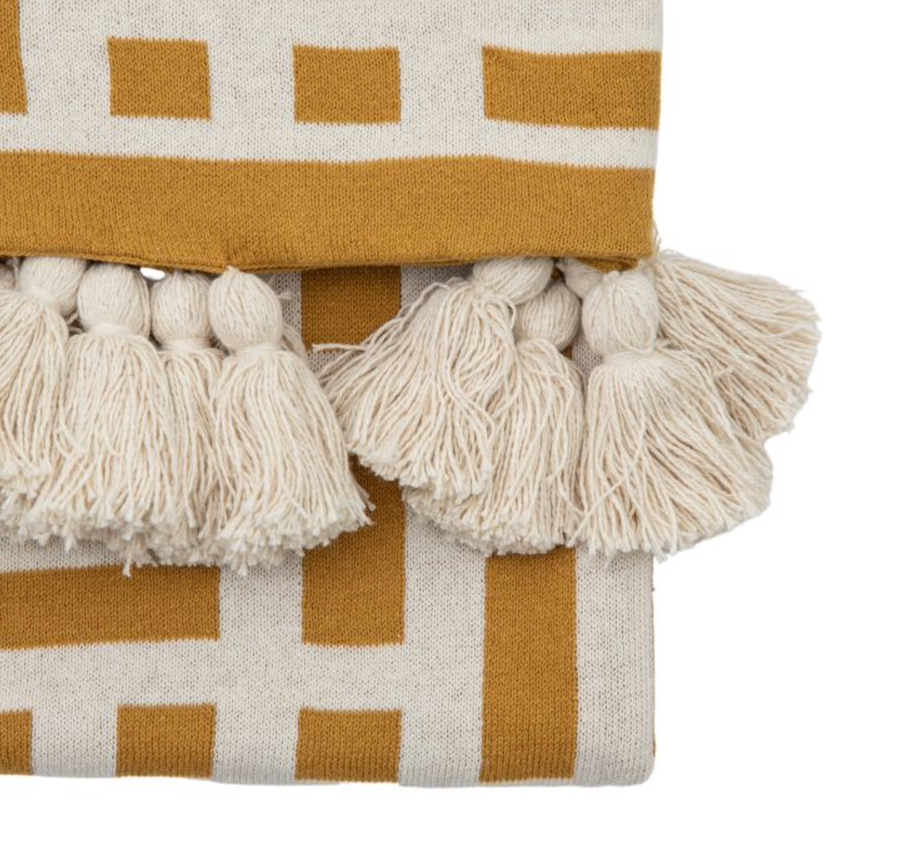 Close-up of a textured fabric with mustard yellow and beige pattern and white tassels.