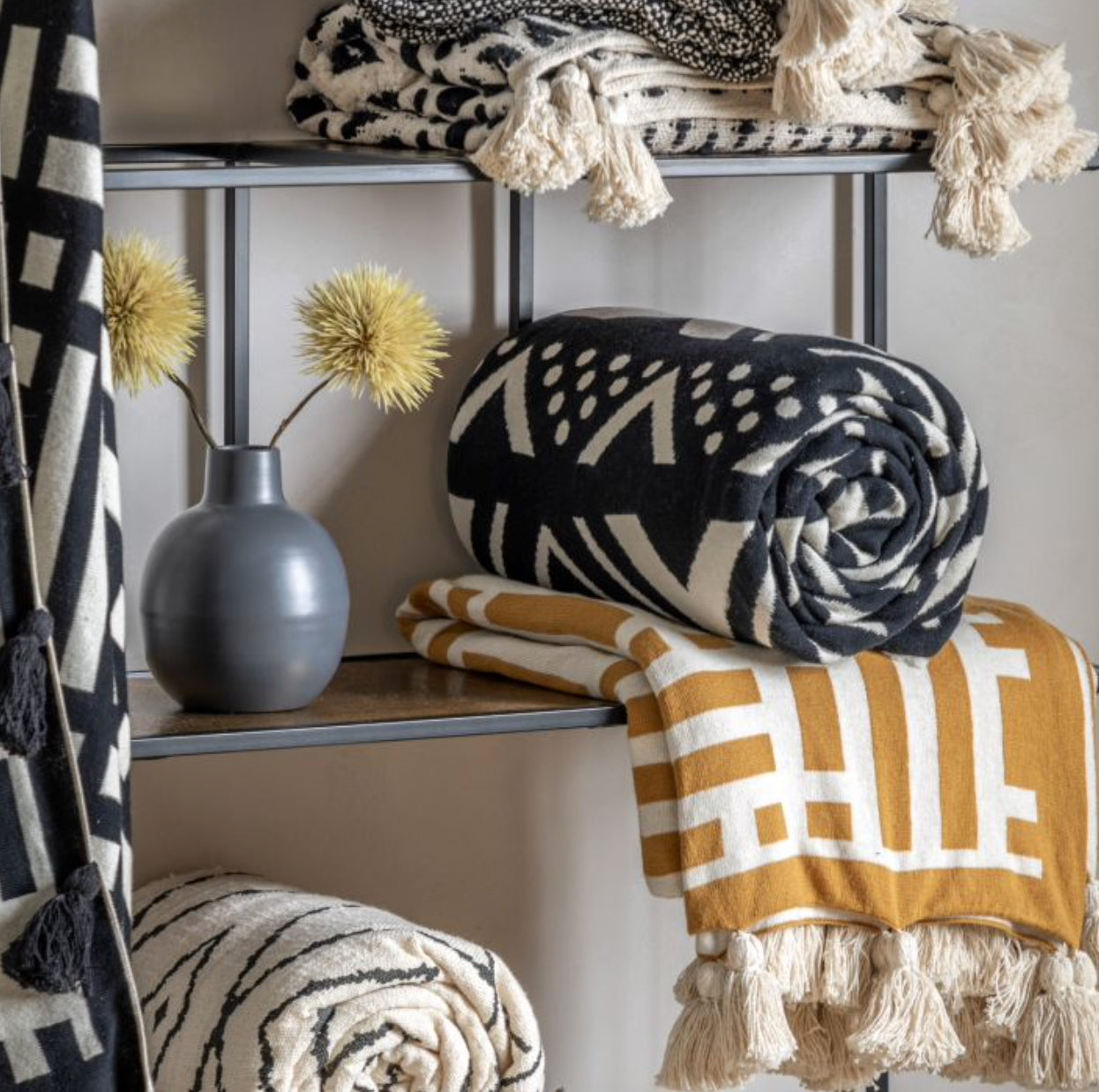 Decorative throw blankets with patterns and colors on a shelf against a neutral wall.