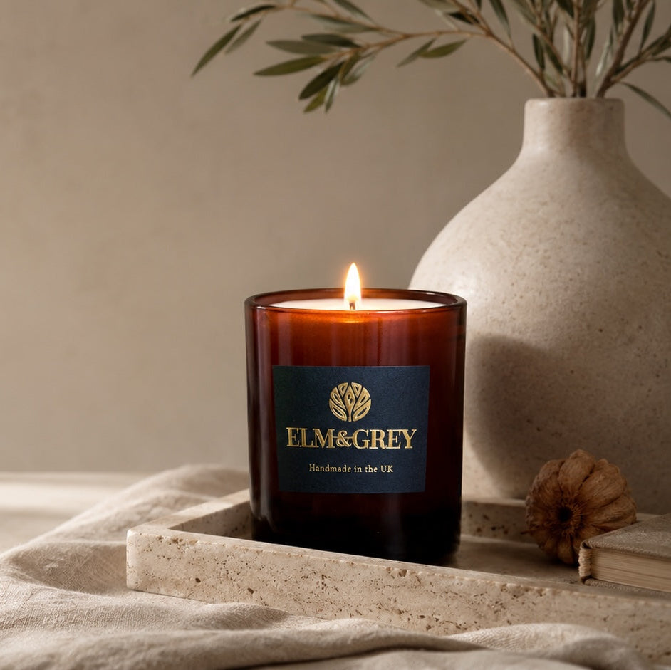 elm and grey luxury scented candle which is lit on a tray with a cream vasee and olive branches behind