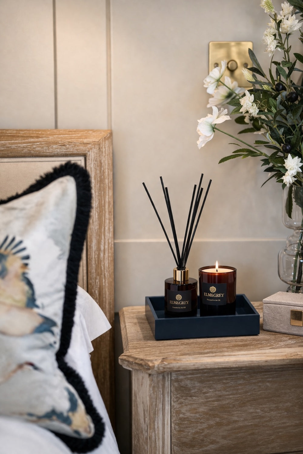 Midnight blue high gloss lacquer square tray on an oak bedside table with Elm & Grey reed diffuser and lit candle beside a glass vase of white flowers and botanical pillow — Elm & Grey