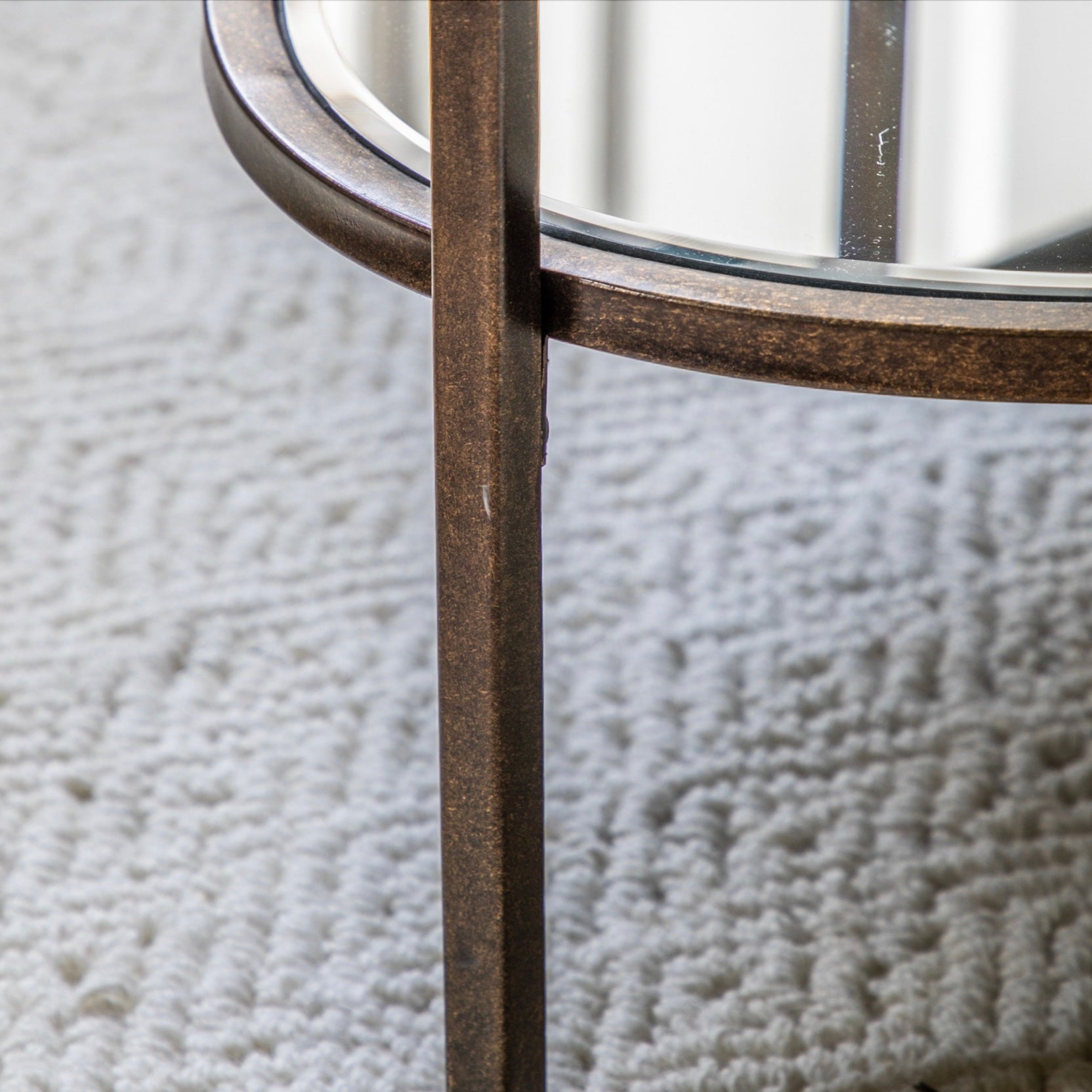 Close-up of an oval  glass coffee table with metal legs on a textured gray surface