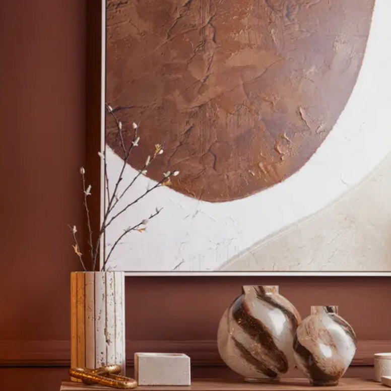 Decorative shelf with mocha swirl vases, books, and a lamp against a brown wall.