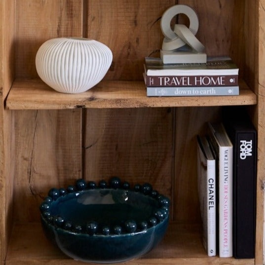 A teal bobble bowl on a rustic set of shelves alongside books from chanel and tom ford