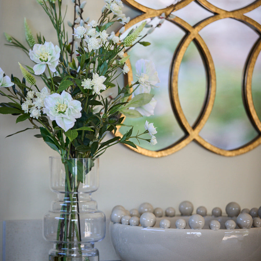 Cream bobble bowl on a side board next to a faux flower arrnagement and mirror