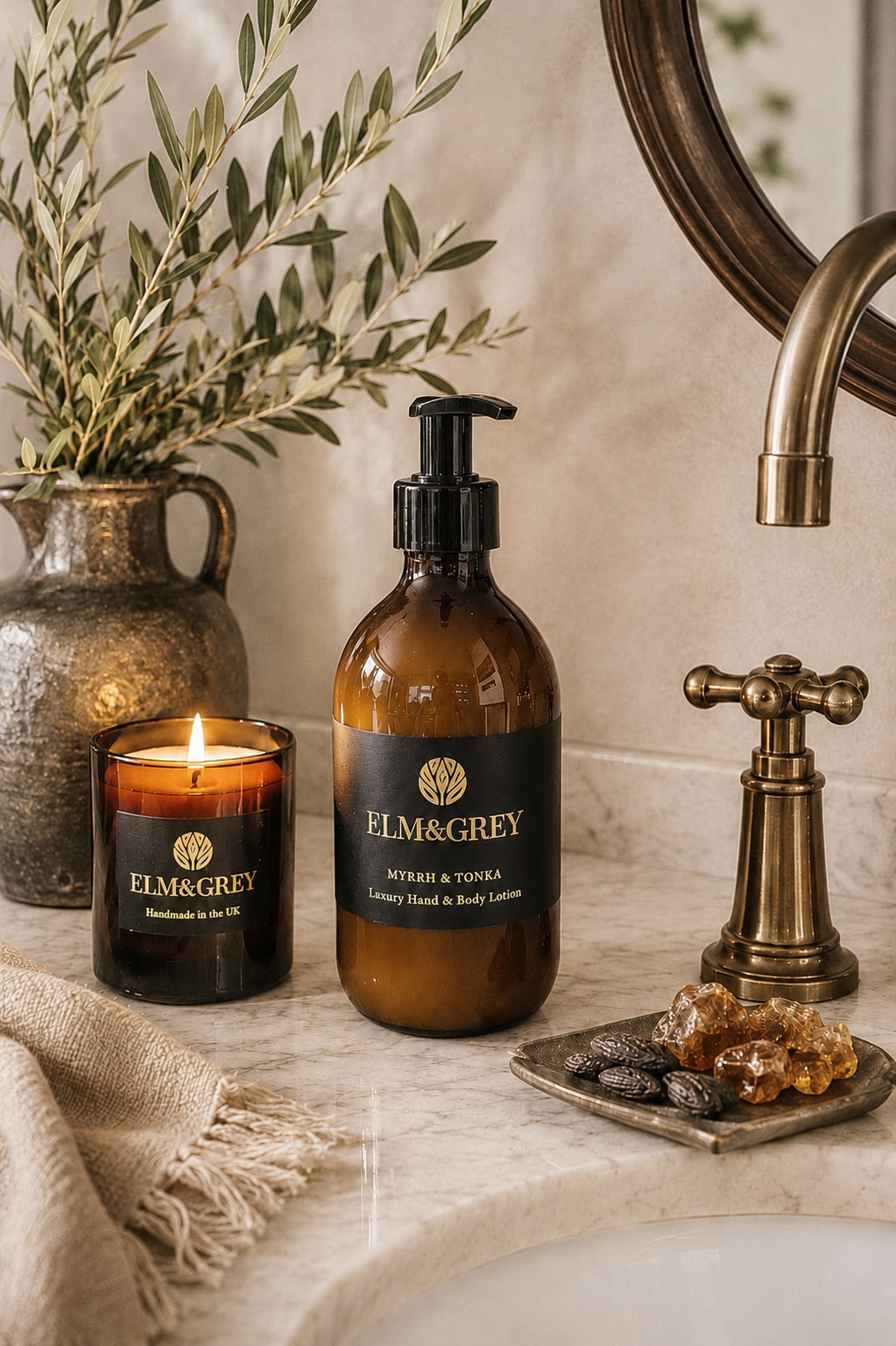 Elm & Grey Myrrh & Tonka hand and body lotion and scented candle styled on a marble bathroom vanity with warm ambient lighting and calming luxury home fragrance.
