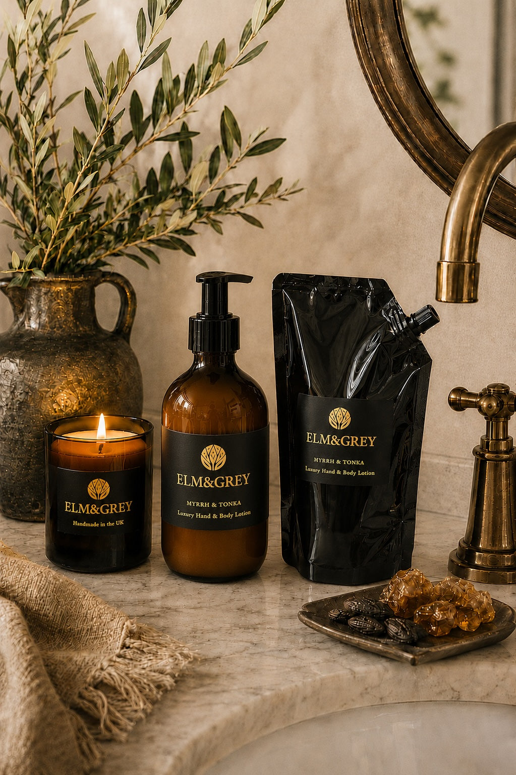 Bathroom setting with Elm & Grey products including a myrrh and tonka candle, hand lotion bottle, and hand lotion refill pouch on a marble surface.