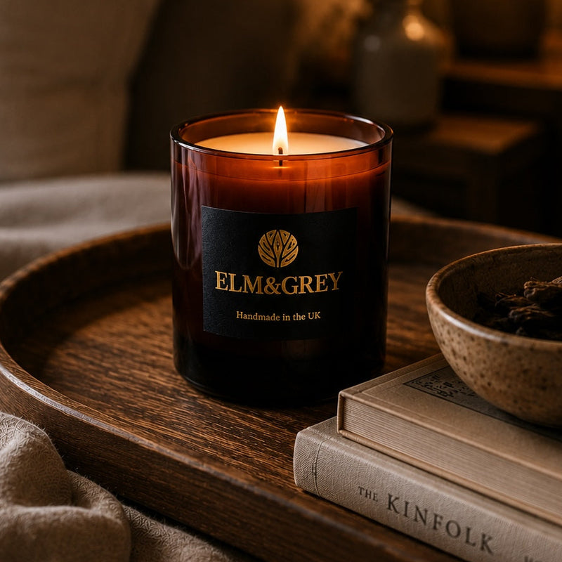 Candle in a brown holder on a wooden tray with books and a bowl in a cozy room setting.