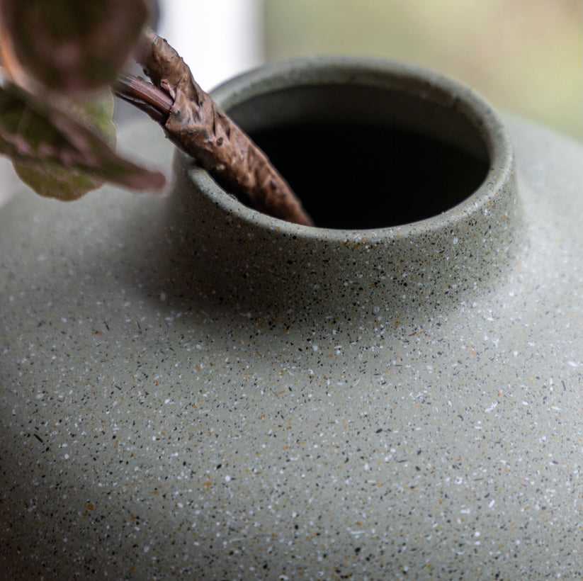 Close-up of a textured olive green  matte vase with a branch inside.