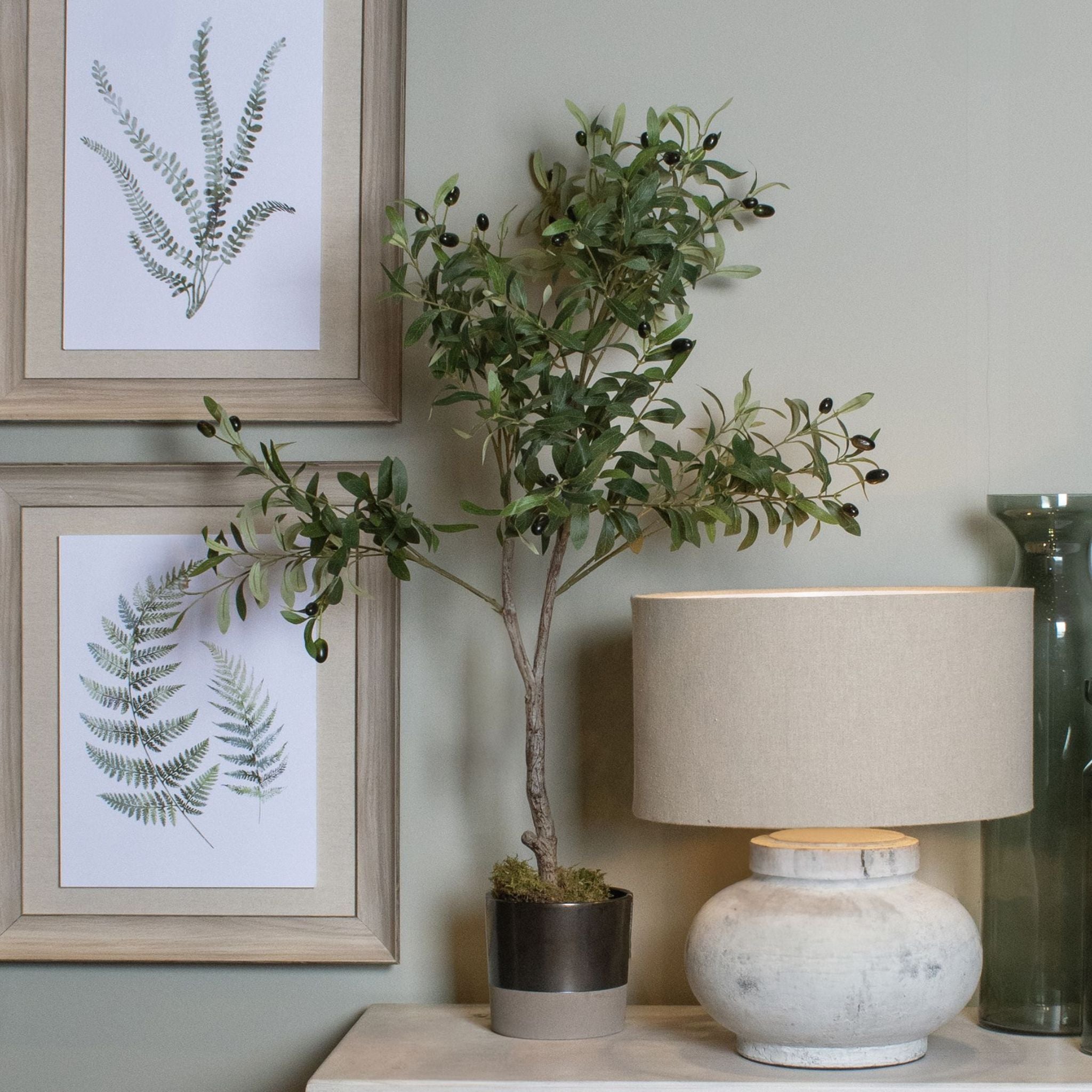 Decorative setup with a potted plant, lamp, and framed artwork on a shelf.