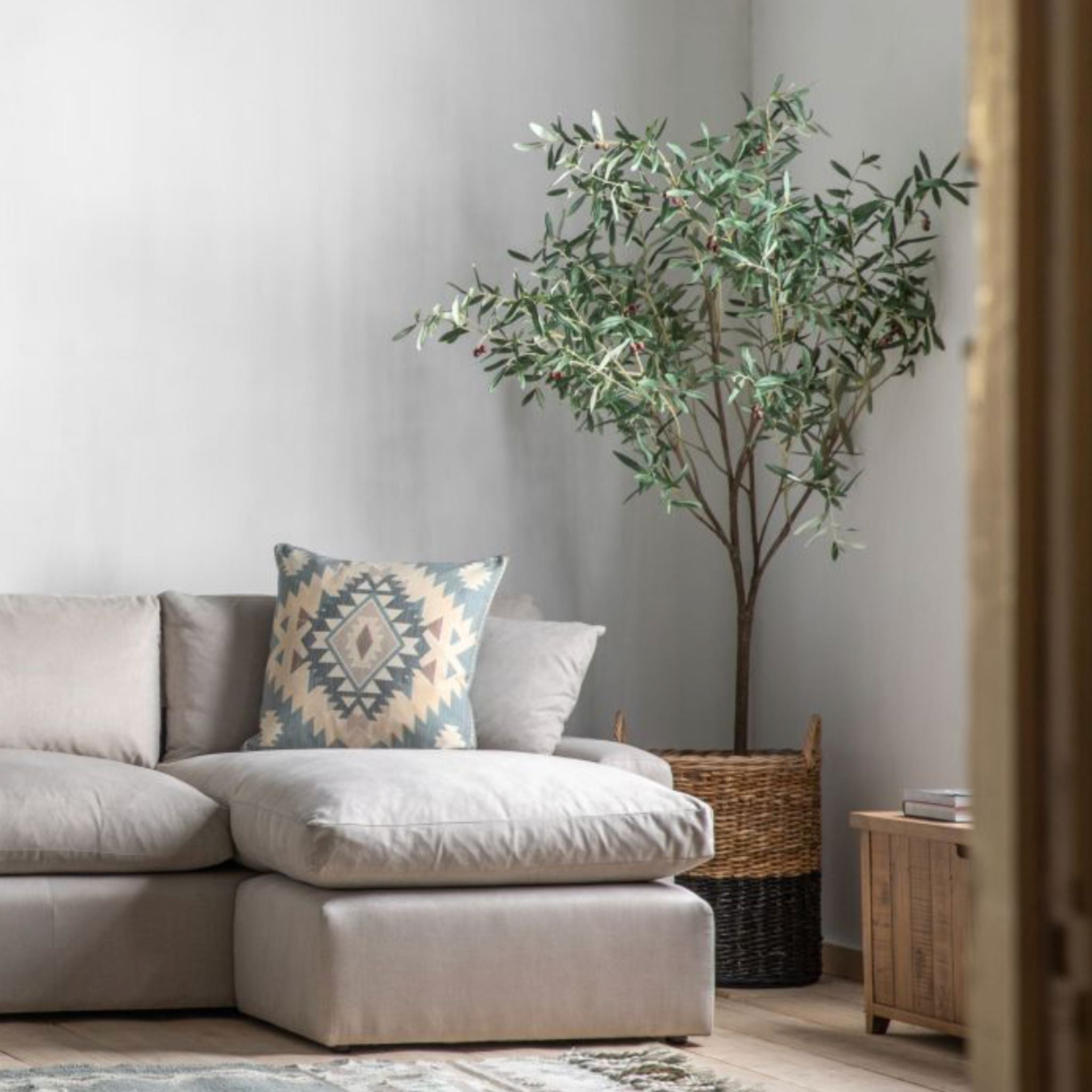 Living room with a beige sectional sofa, decorative pillow, and a potted plant.