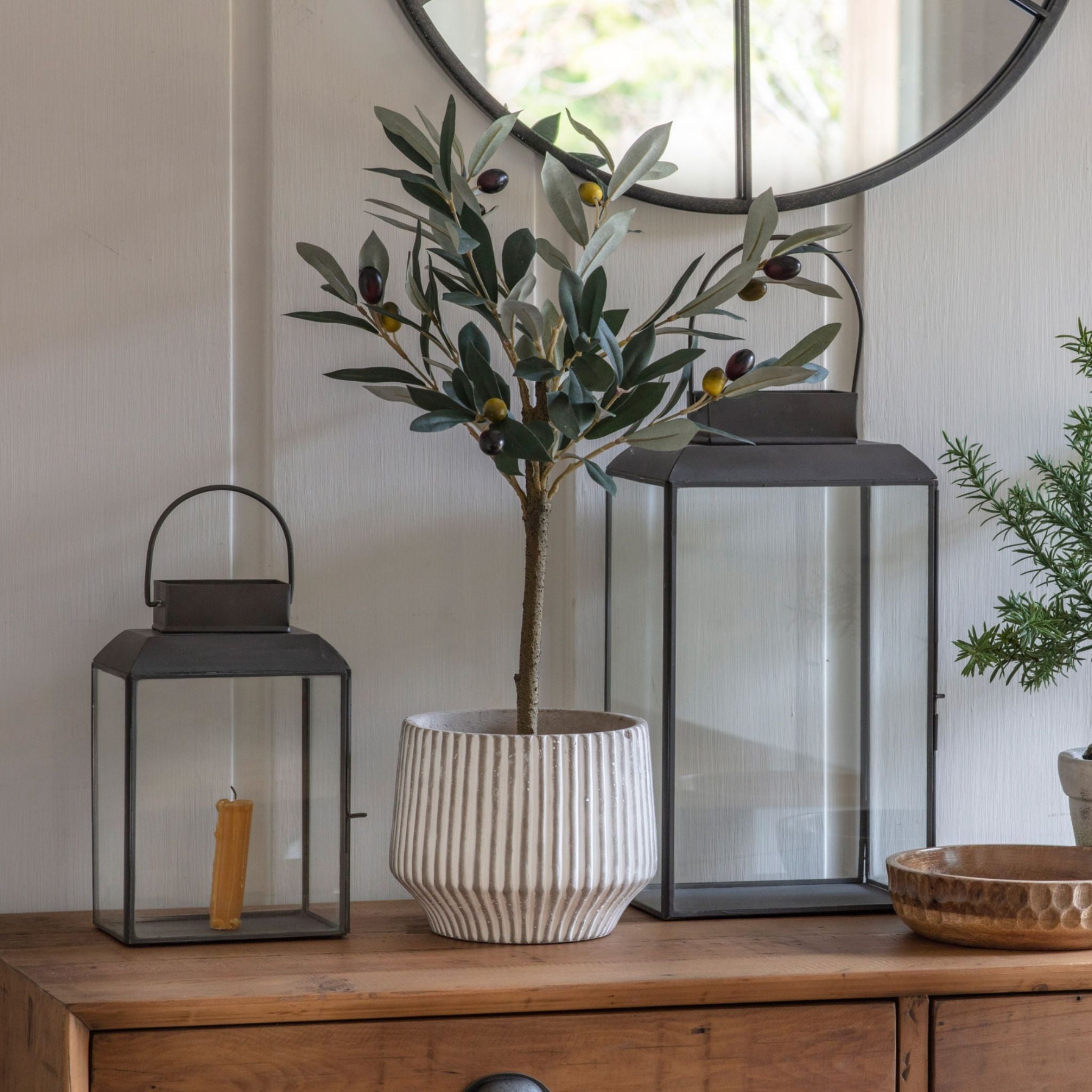 Decorative setup with a potted plant, lanterns, and a mirror on a wooden surface.