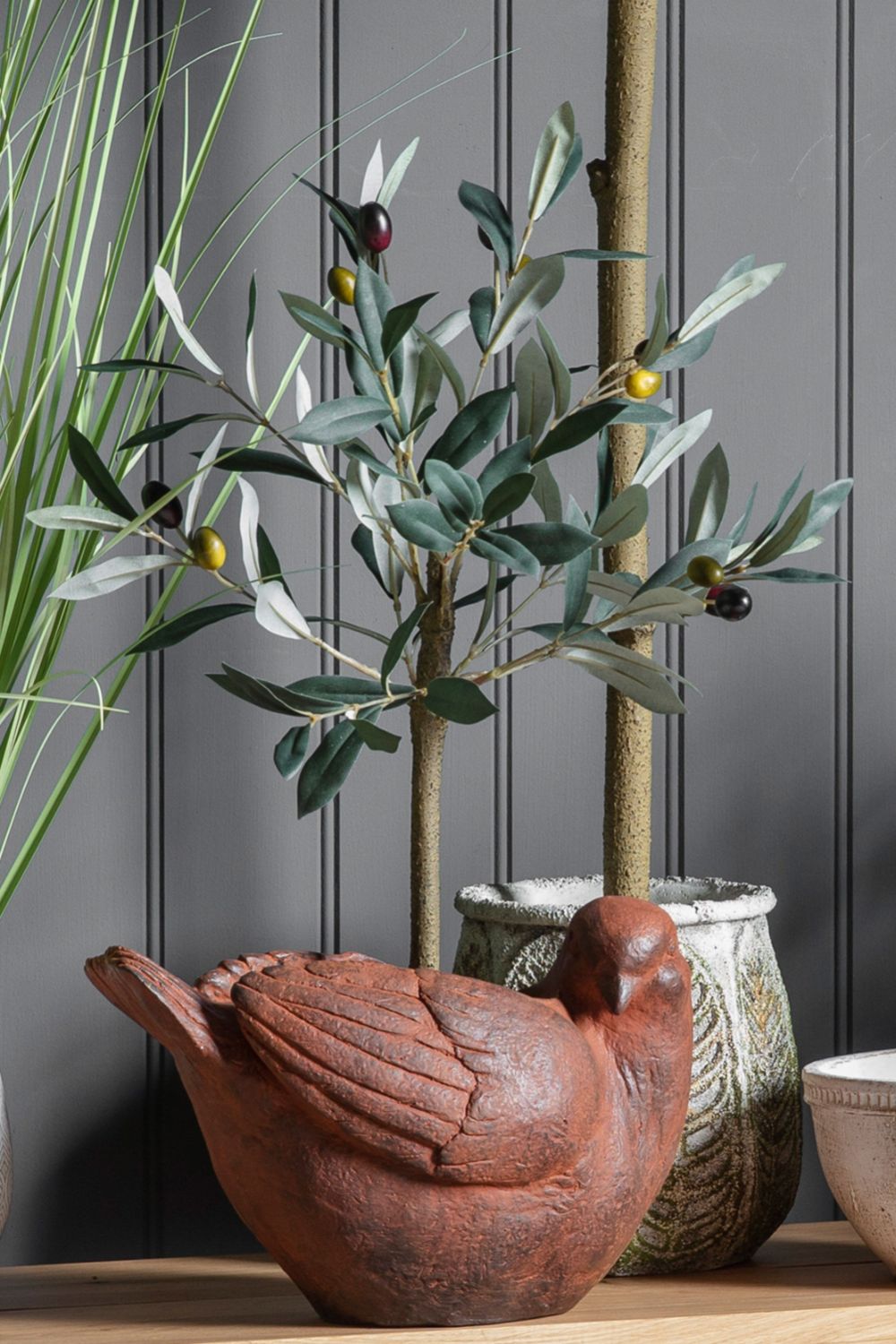 Decorative terracotta chicken with a plant and vase on a wooden surface against a gray wall.