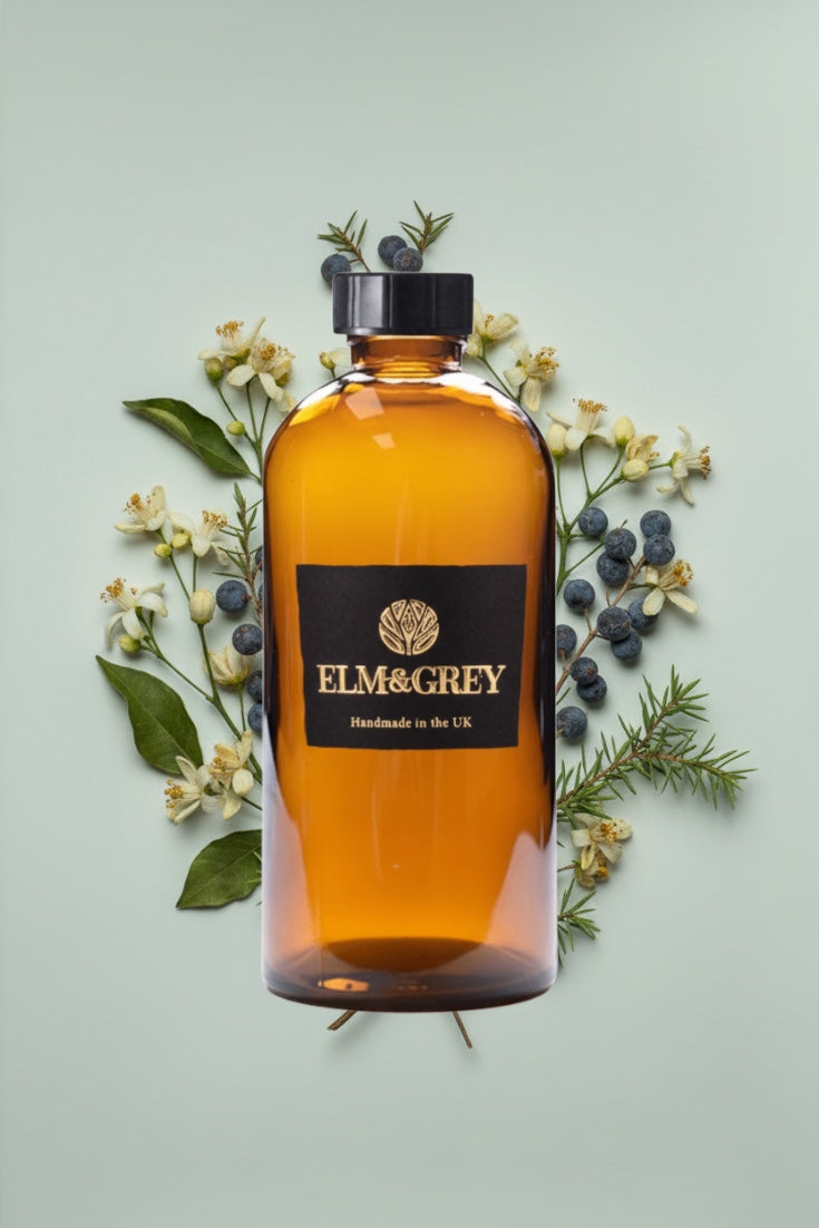 Bottle of Elm & Grey diffuser refill liquid on a light green background with flowers and berries