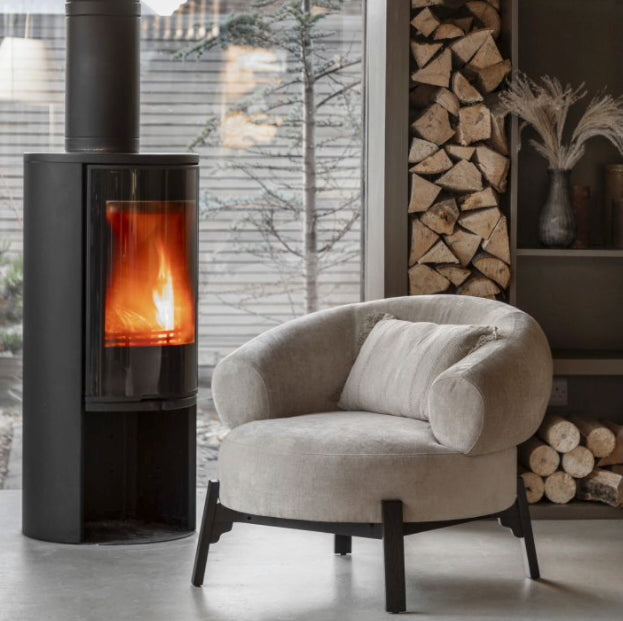 Modern curved armchair in a room with a stove and stacked firewood, Elm & Grey.