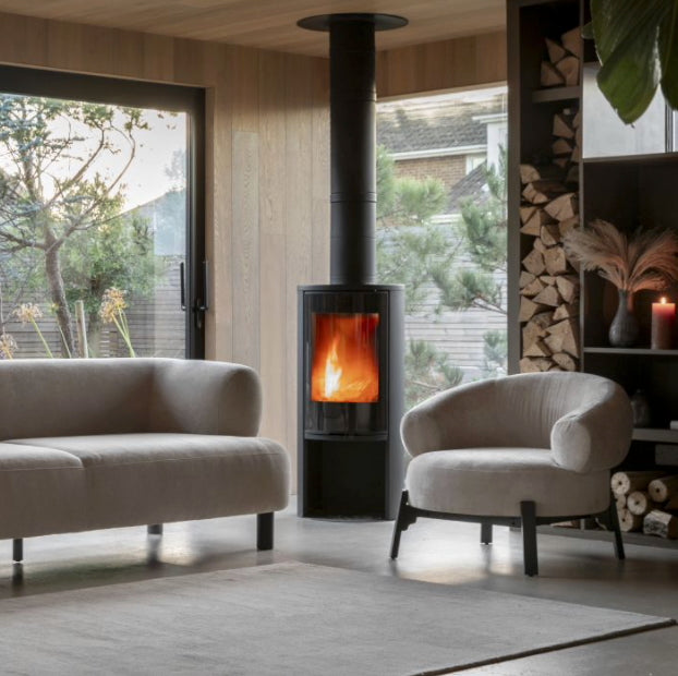 Modern curved armchair in a room with a stove and stacked firewood, Elm & Grey.