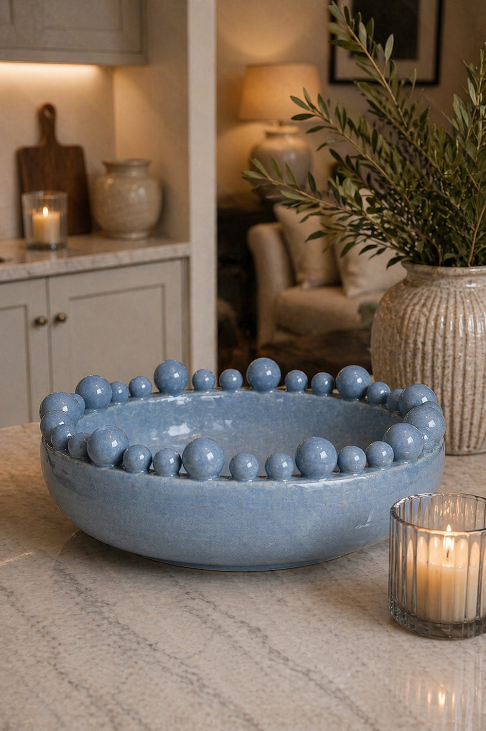 Powder blue bobble-edged ceramic decorative bowl on marble kitchen counter with lit ribbed tealight and olive branches in ceramic vase — Elm & Grey