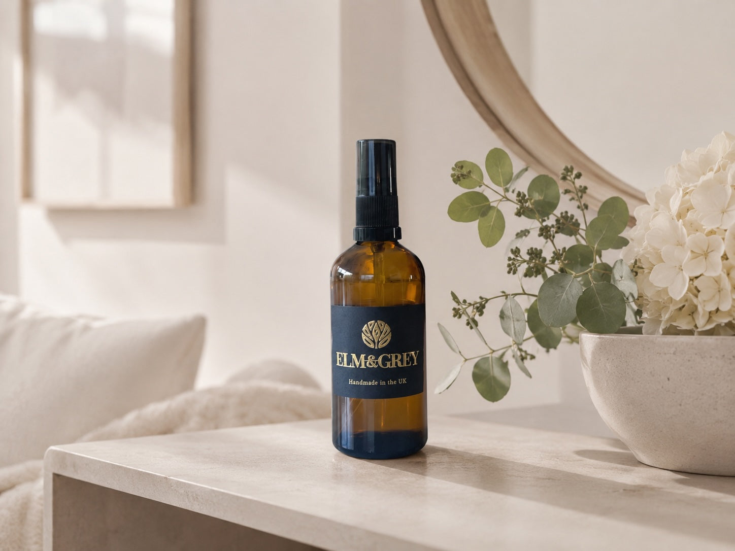 Bottle of Elm & Grey room spray on a table with a decorative plant in the background