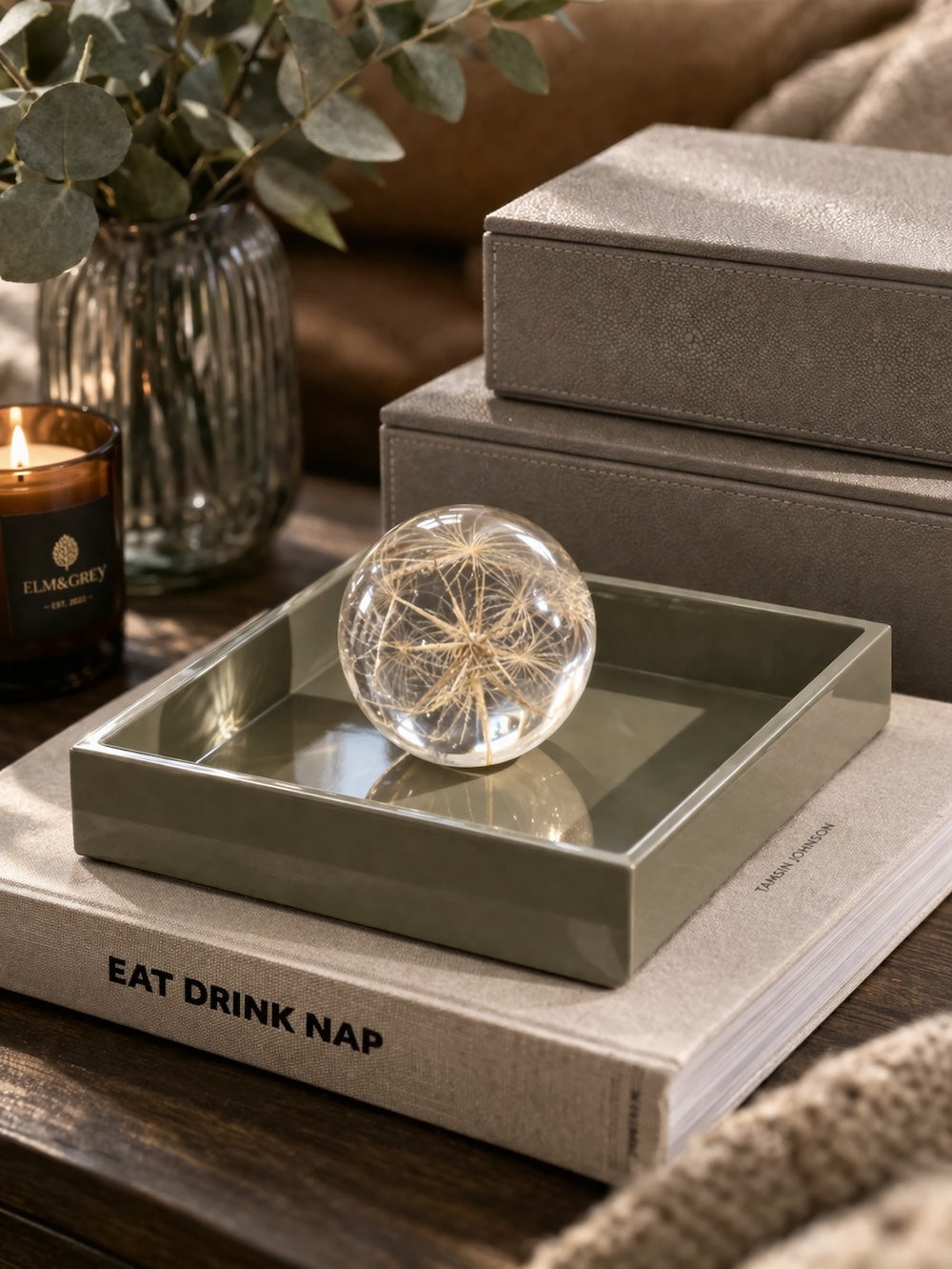 Sage green high gloss lacquer square tray styled with a glass dandelion sphere paperweight on stacked books beside Elm & Grey candle and faux shagreen boxes — Elm & Grey