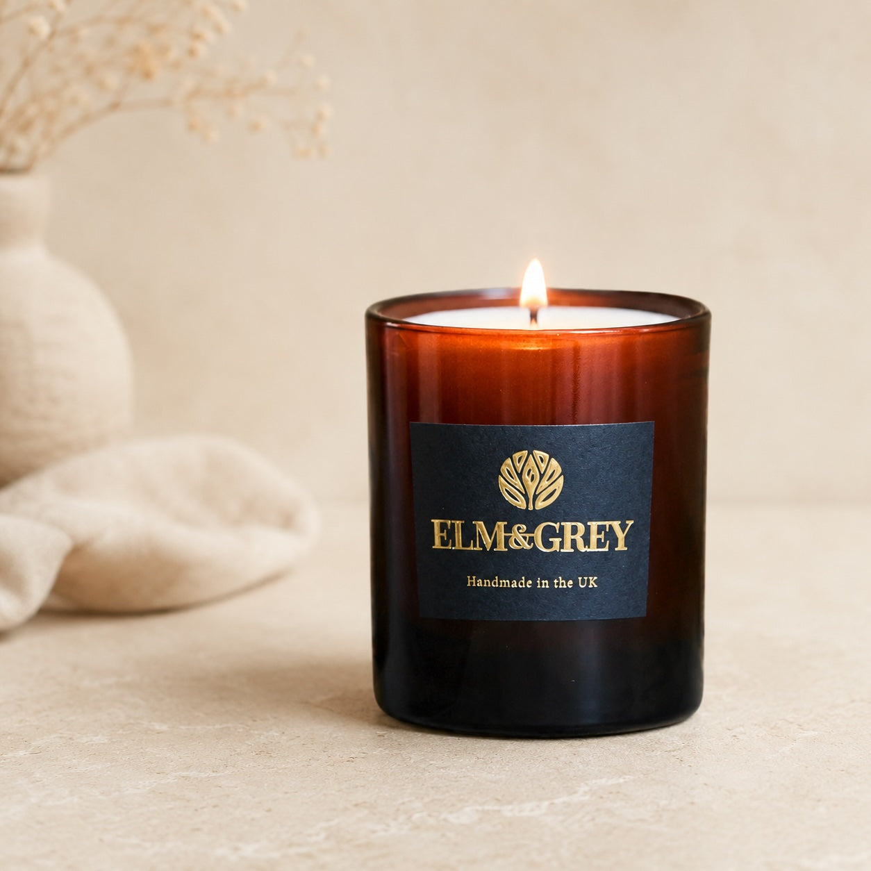 Elm & Grey candle with a lit flame on a neutral background