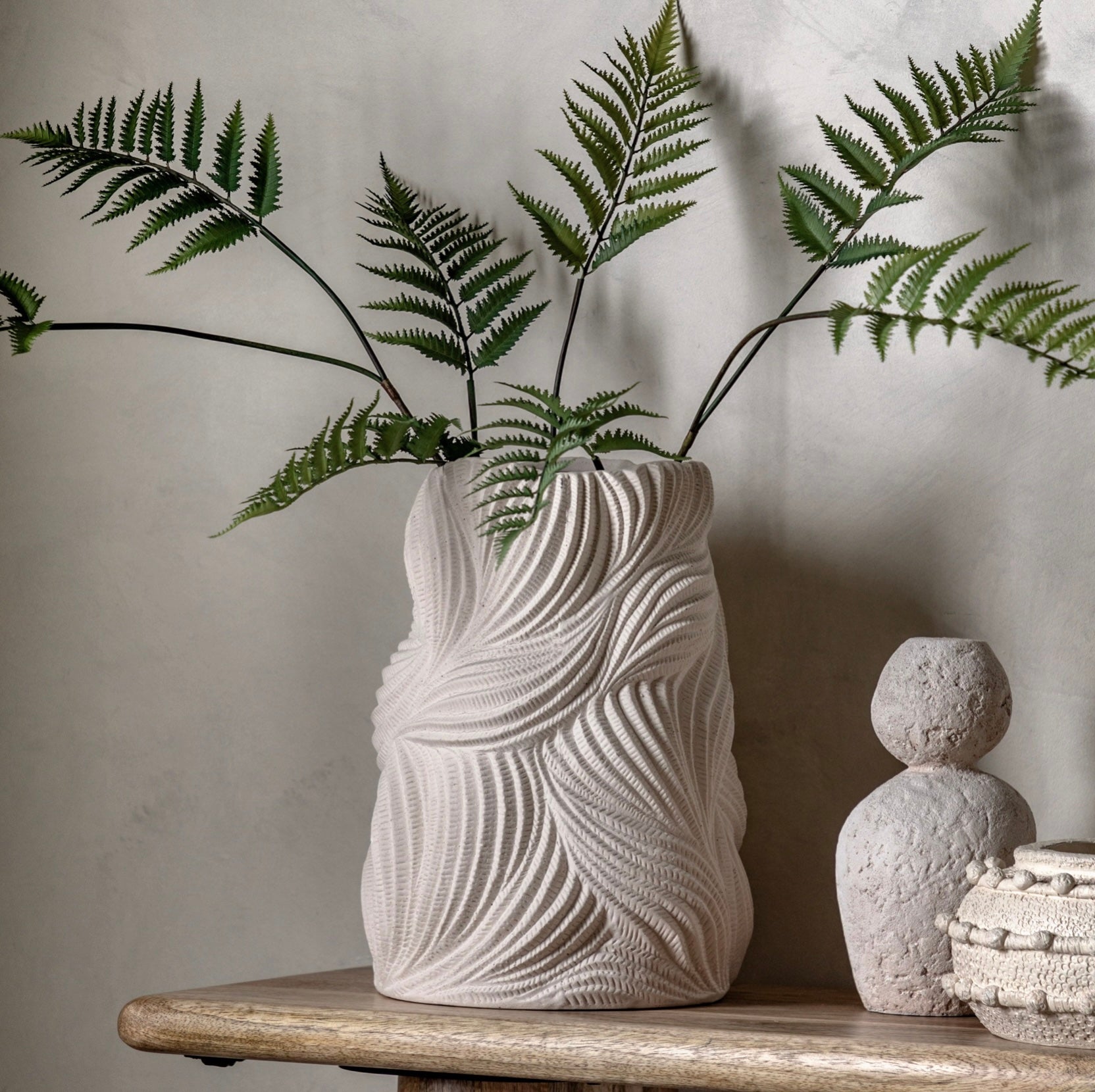 Textured vase with ferns on a wooden surface against a neutral background