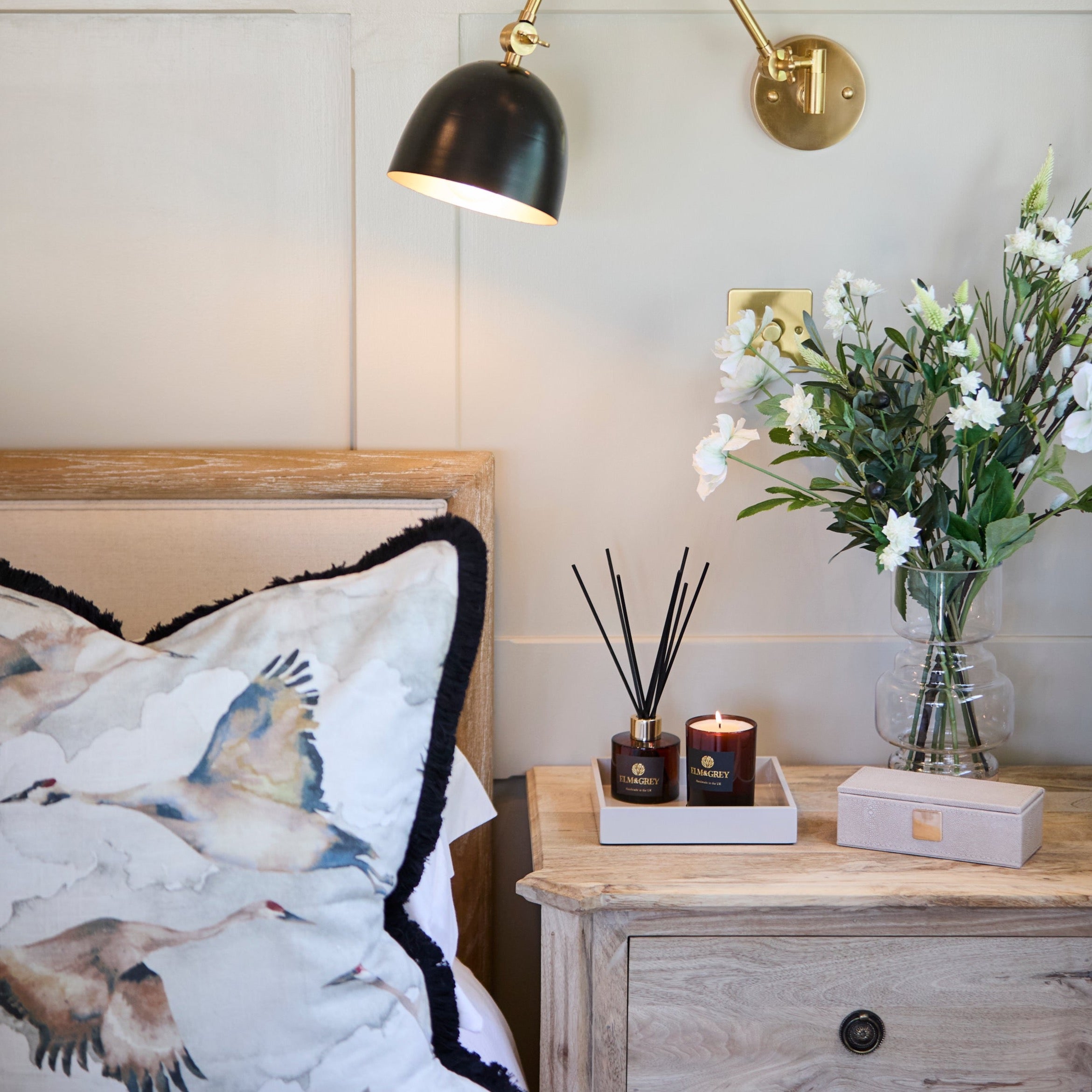 An ivory faux shagreen case with a sophisticated design, placed on a wooden surface, decorated with a floral patterned pillow and a candle.