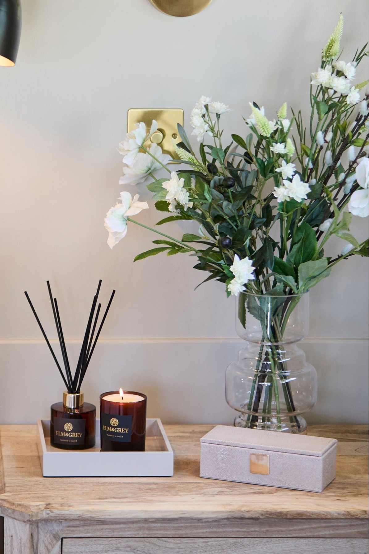 Decorative items including a diffuser, candle, and vase with flowers on a wooden surface.
