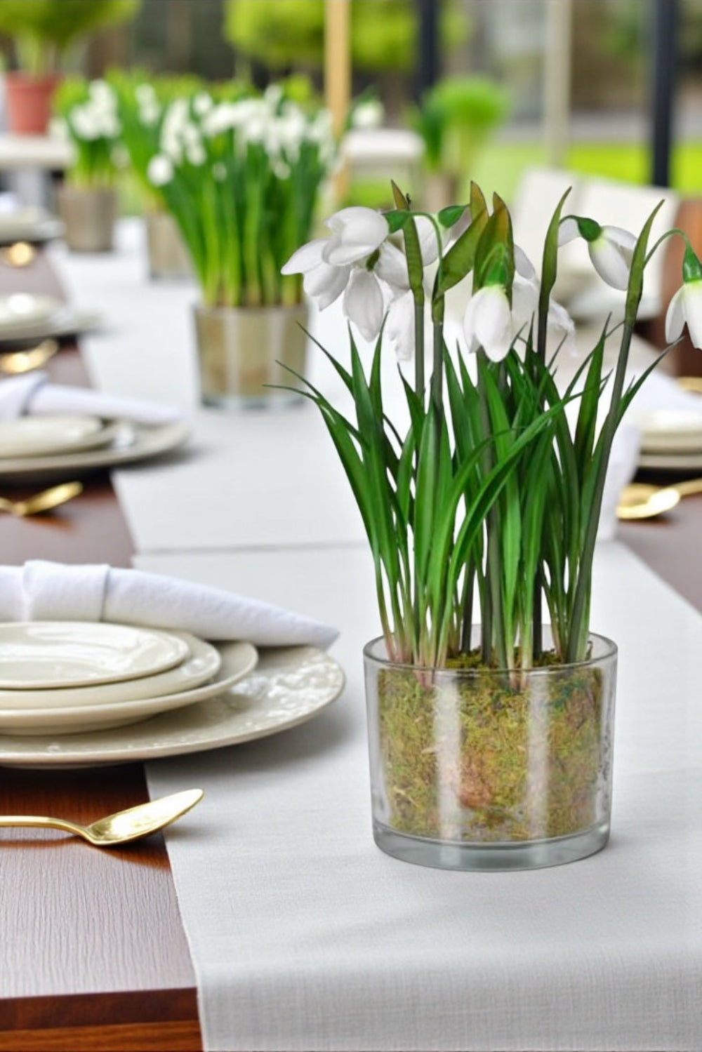Decorative table setting with glass vases containing greenery and white flowers.