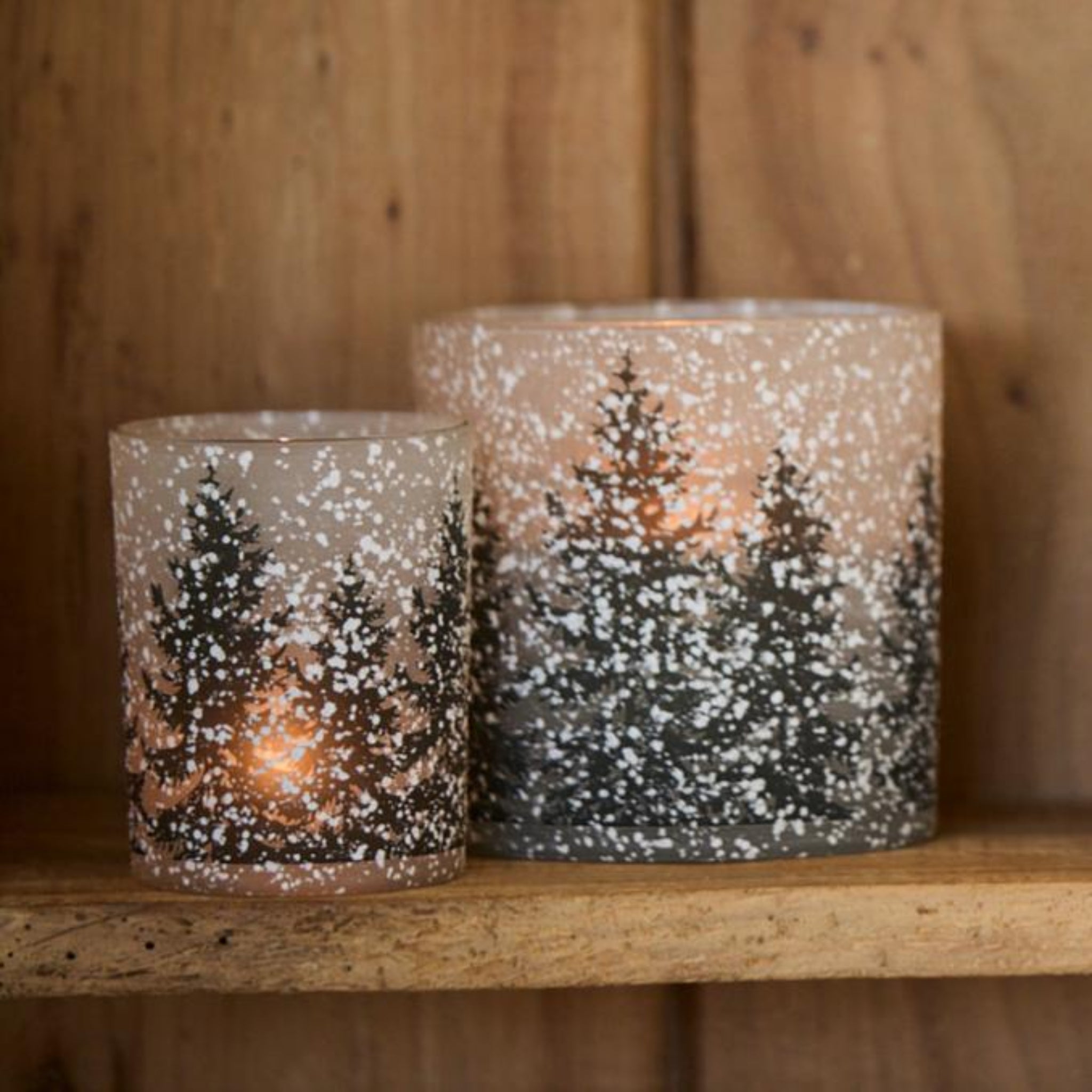Two candle holders with winter scene design on a wooden surface