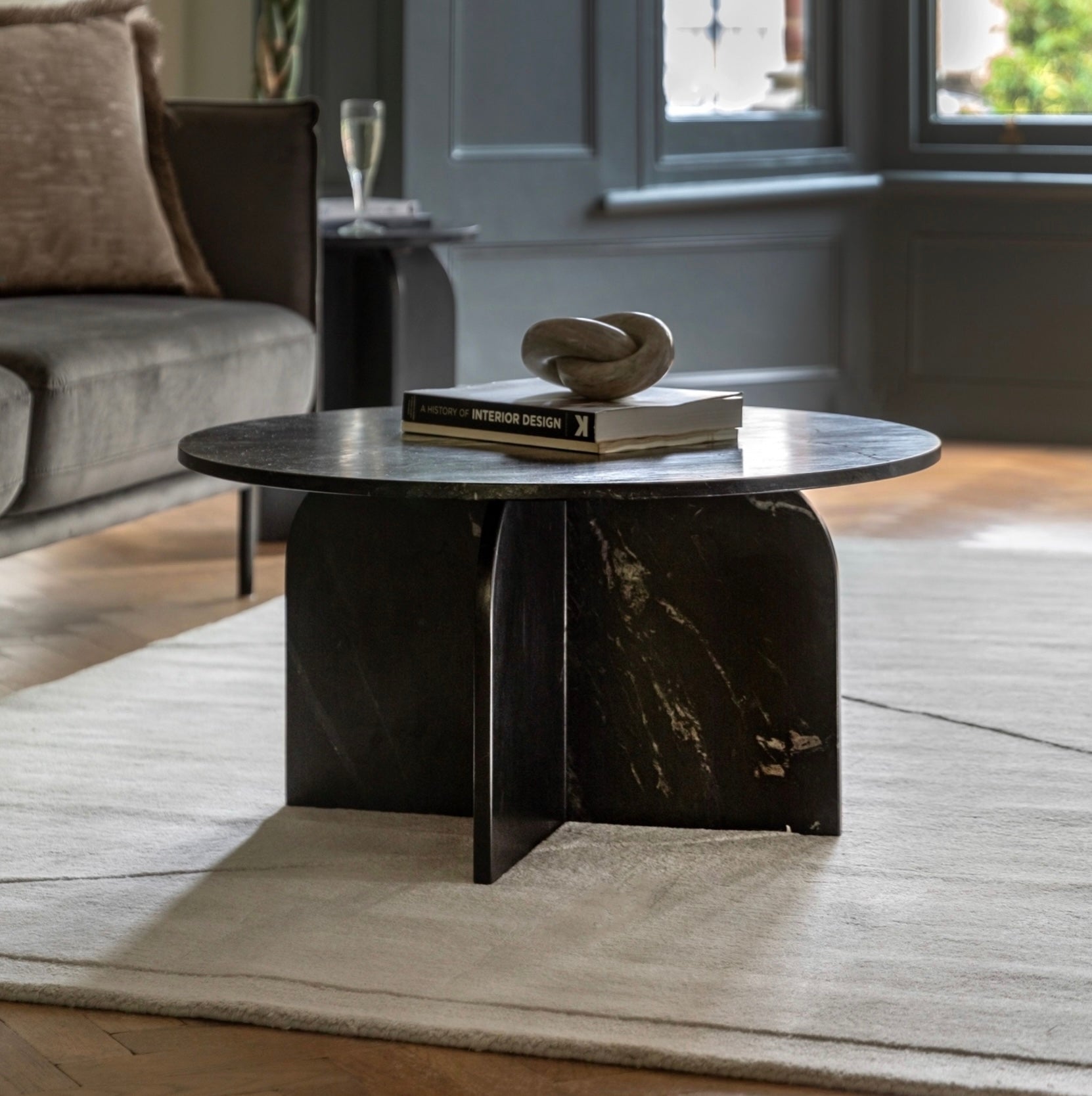 Round black marble coffee table in a living room setting with books and a sculpture on top.