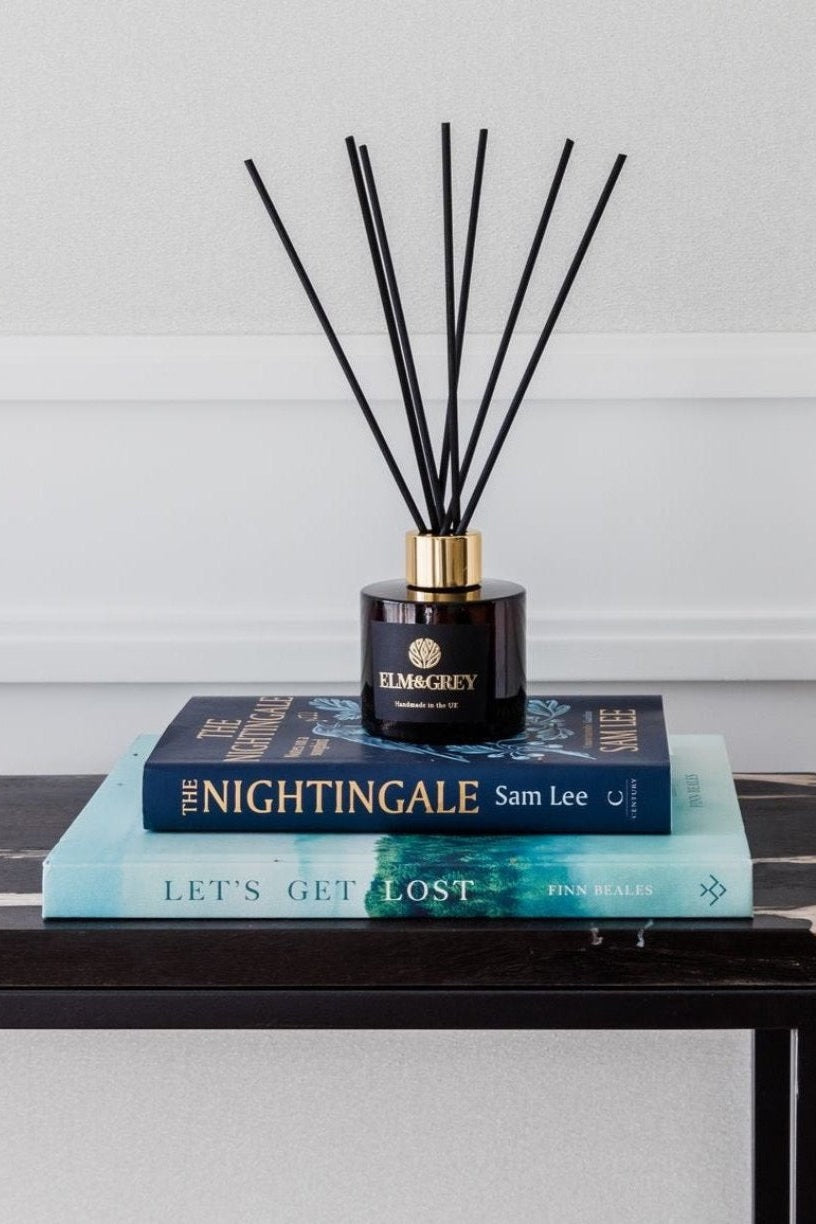 Fragrance diffuser with black sticks on top of books against a light background
